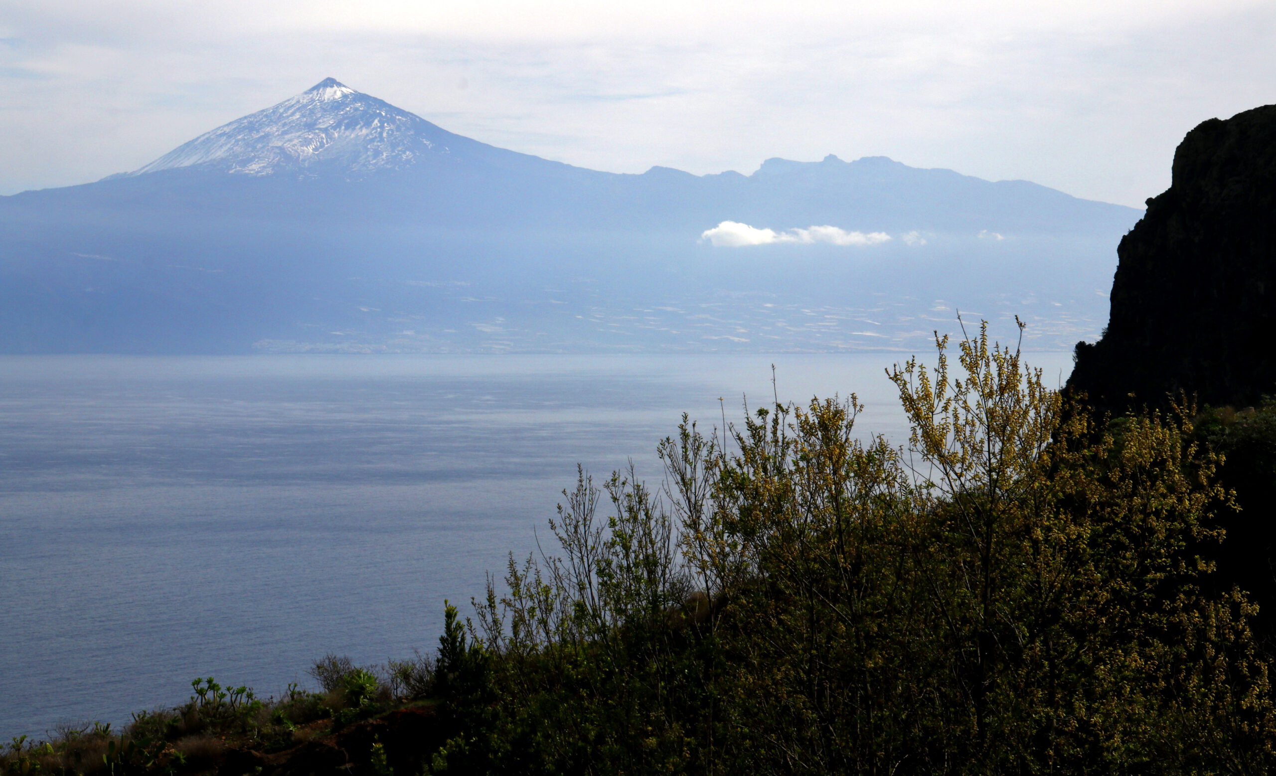 The distinctive cone of Teide volcano on Tenerife dominates the horizon from Mirador de Abrante, with the Atlantic stretching below and La Gomera's rugged terrain framing the view.