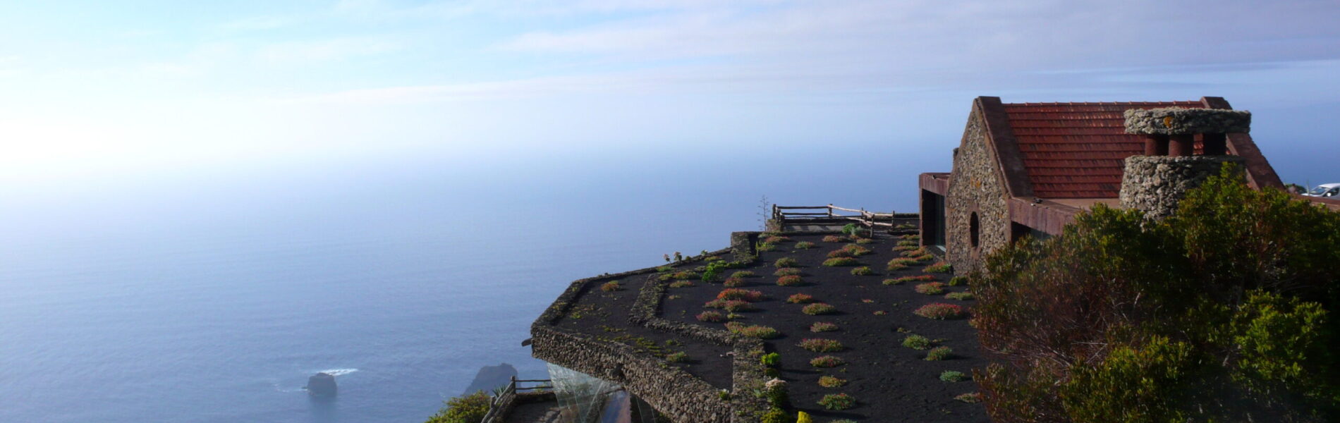 Stone building with red-tile roof on volcanic cliff overlooking deep blue ocean