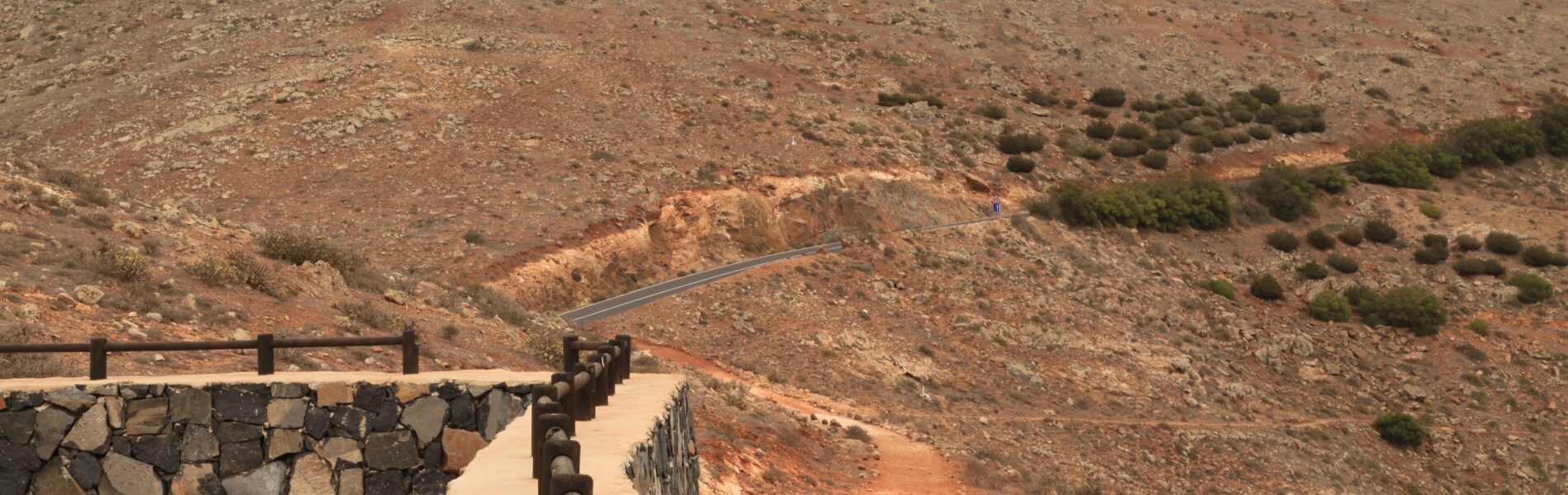Viewing platform with stone railing overlooking a bare, rocky hill dotted with sparse vegetation under clear sky