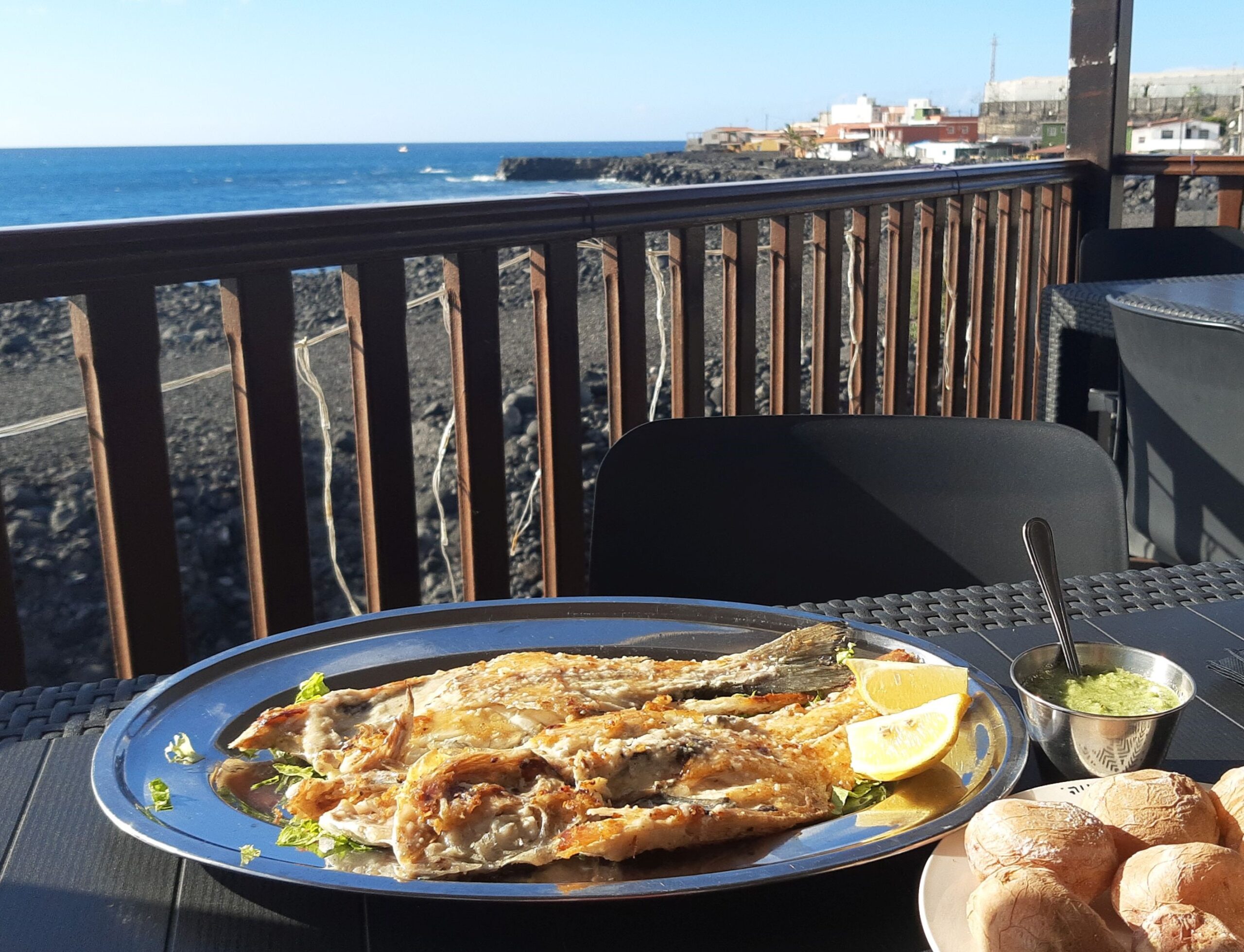 Fresh grilled fish with mojo verde sauce served at a beachfront restaurant with views of the Atlantic coast.