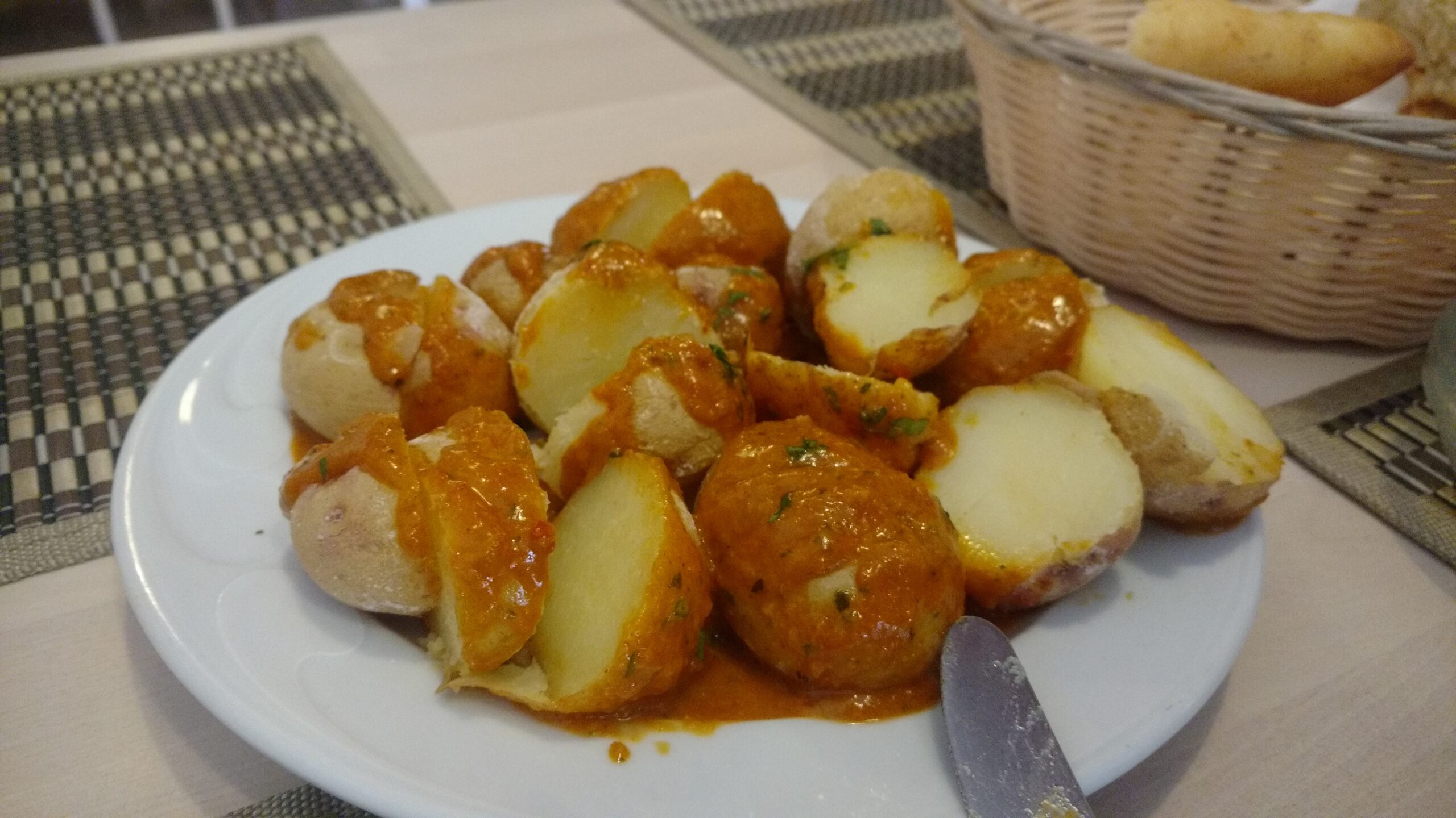 Plate of papas arrugadas, small wrinkled potatoes roasted golden brown with herbs and seasoning, served on a white plate with a fork at a restaurant table.