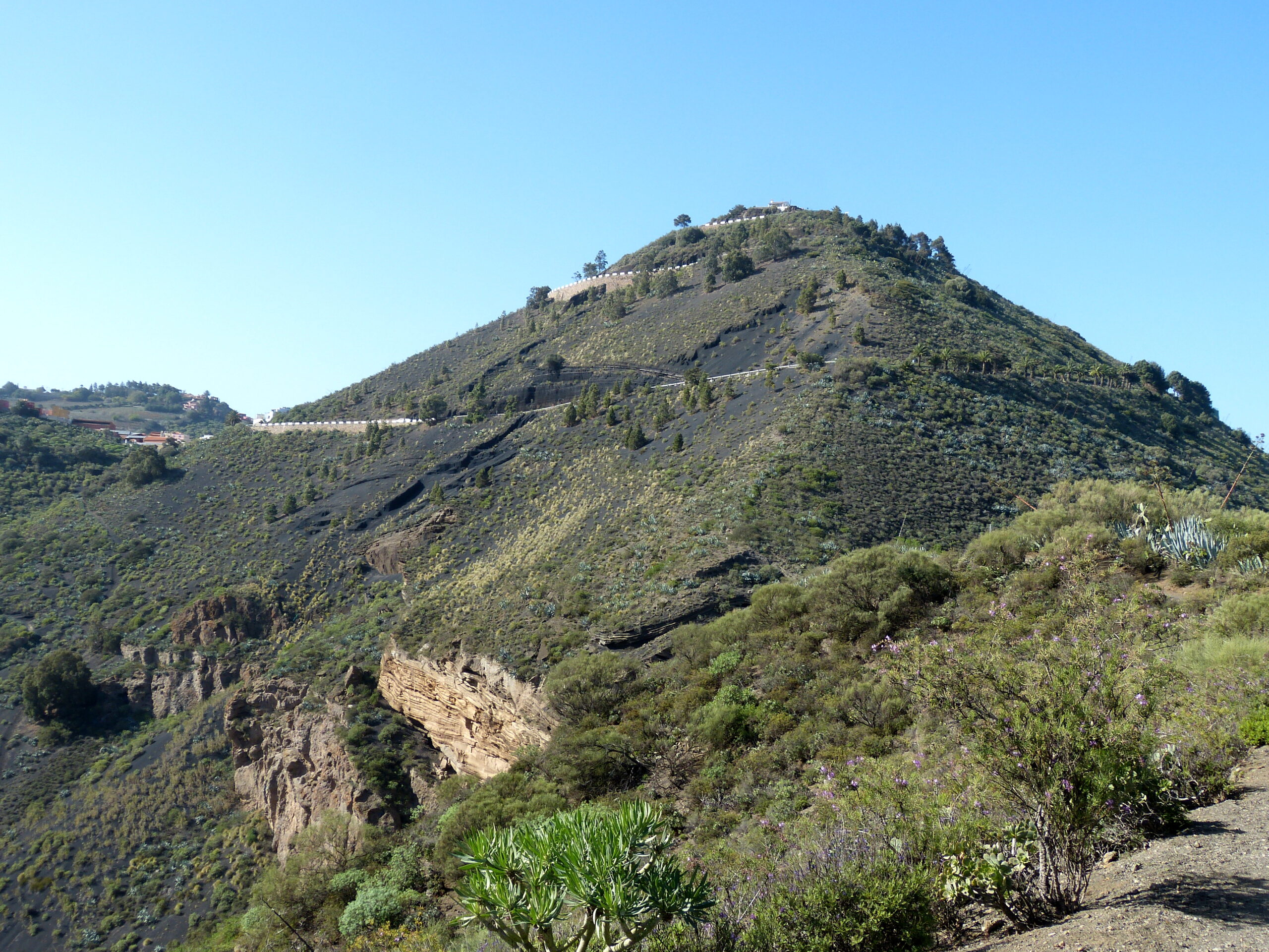 Pico de Bandama rises prominently above the surrounding landscape, its slopes covered in endemic vegetation with rocky outcrops visible throughout.