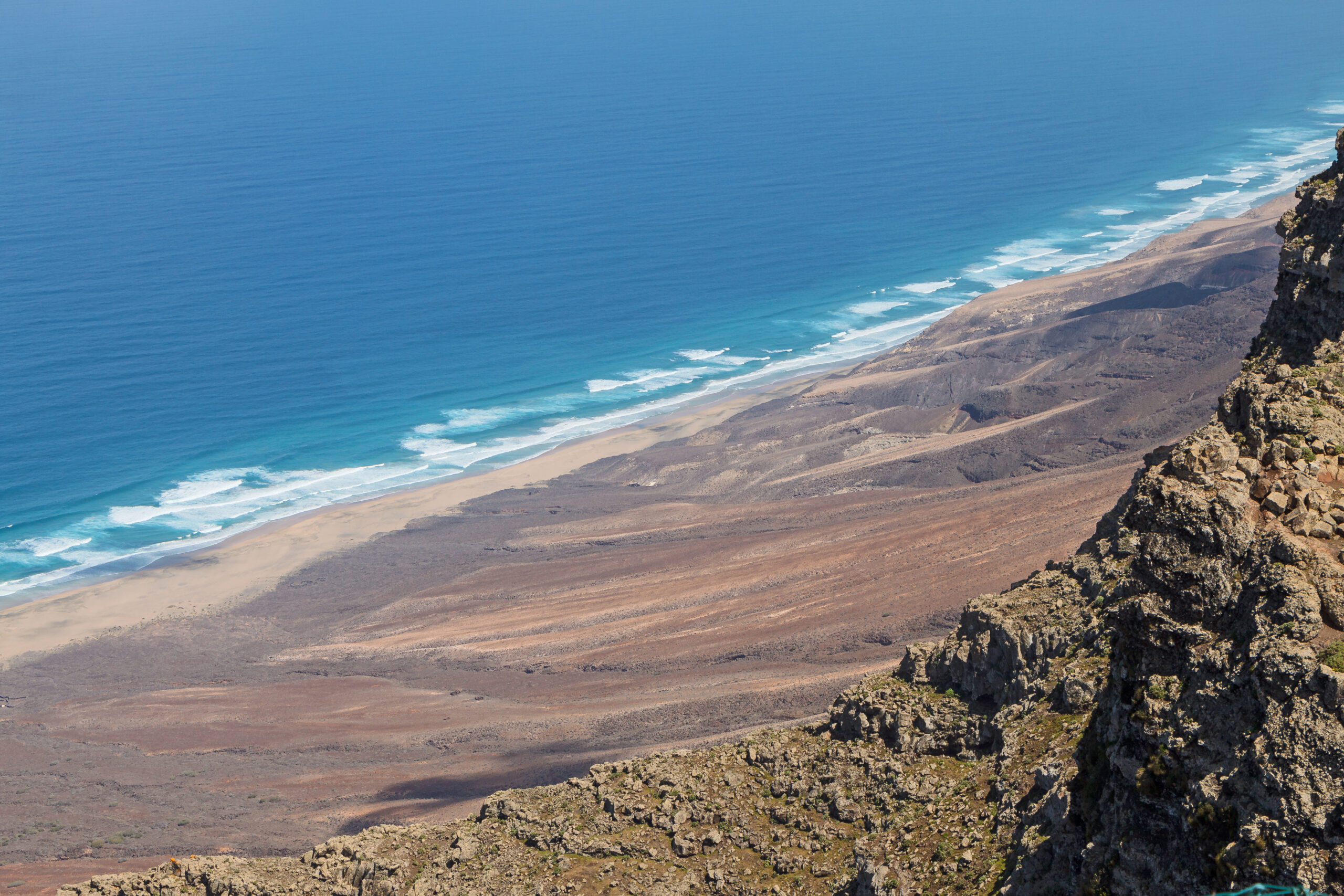 The dramatic coastline of Jandía stretches below, with golden sand meeting rolling volcanic terrain visible from the elevated vantage point at Pico de la Zarza.