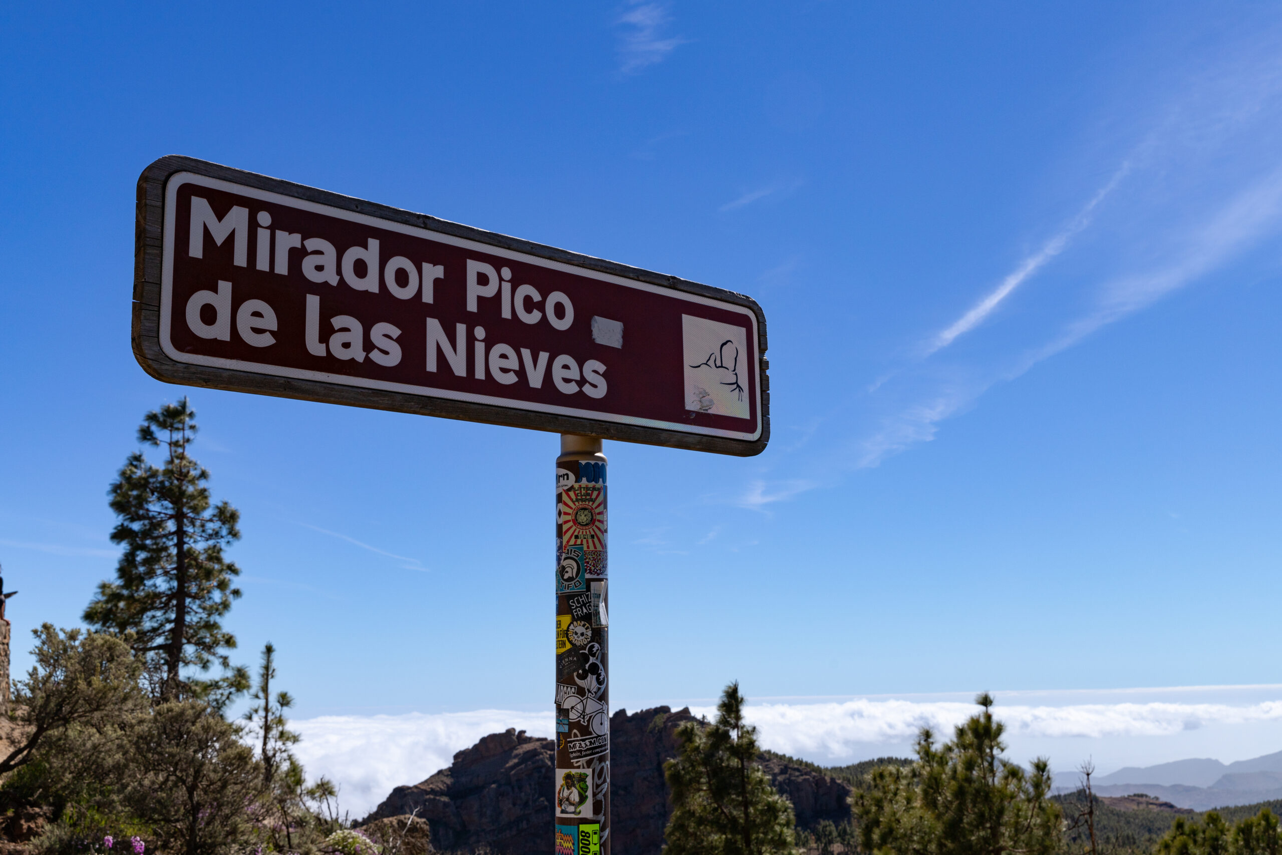 The directional sign for Mirador Pico de las Nieves, the viewpoint at Gran Canaria's highest peak, set against the island's mountainous terrain.