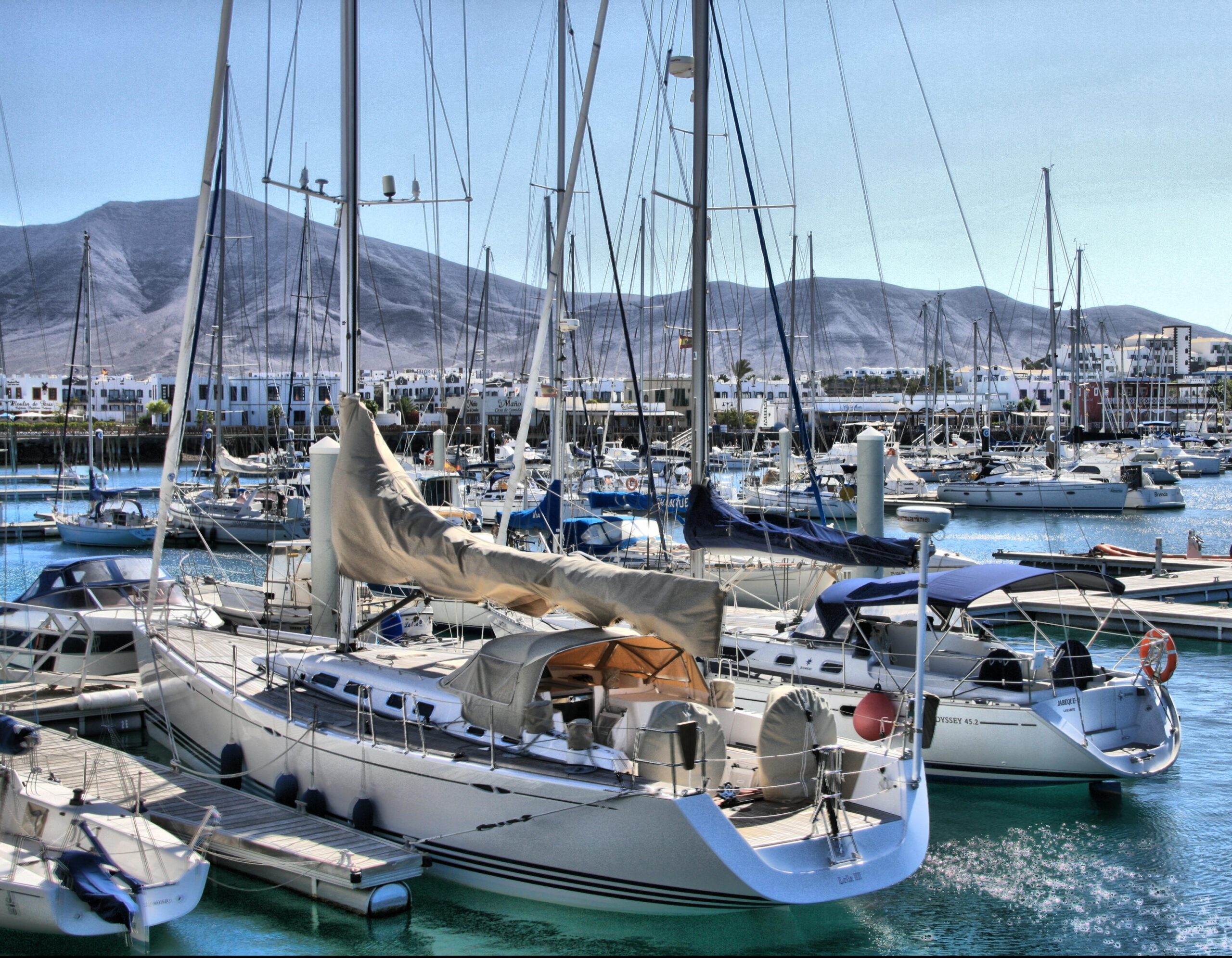 The marina at Playa Blanca features a working fleet of sailboats anchored in clear turquoise waters, with the village's whitewashed architecture and volcanic landscape rising behind.