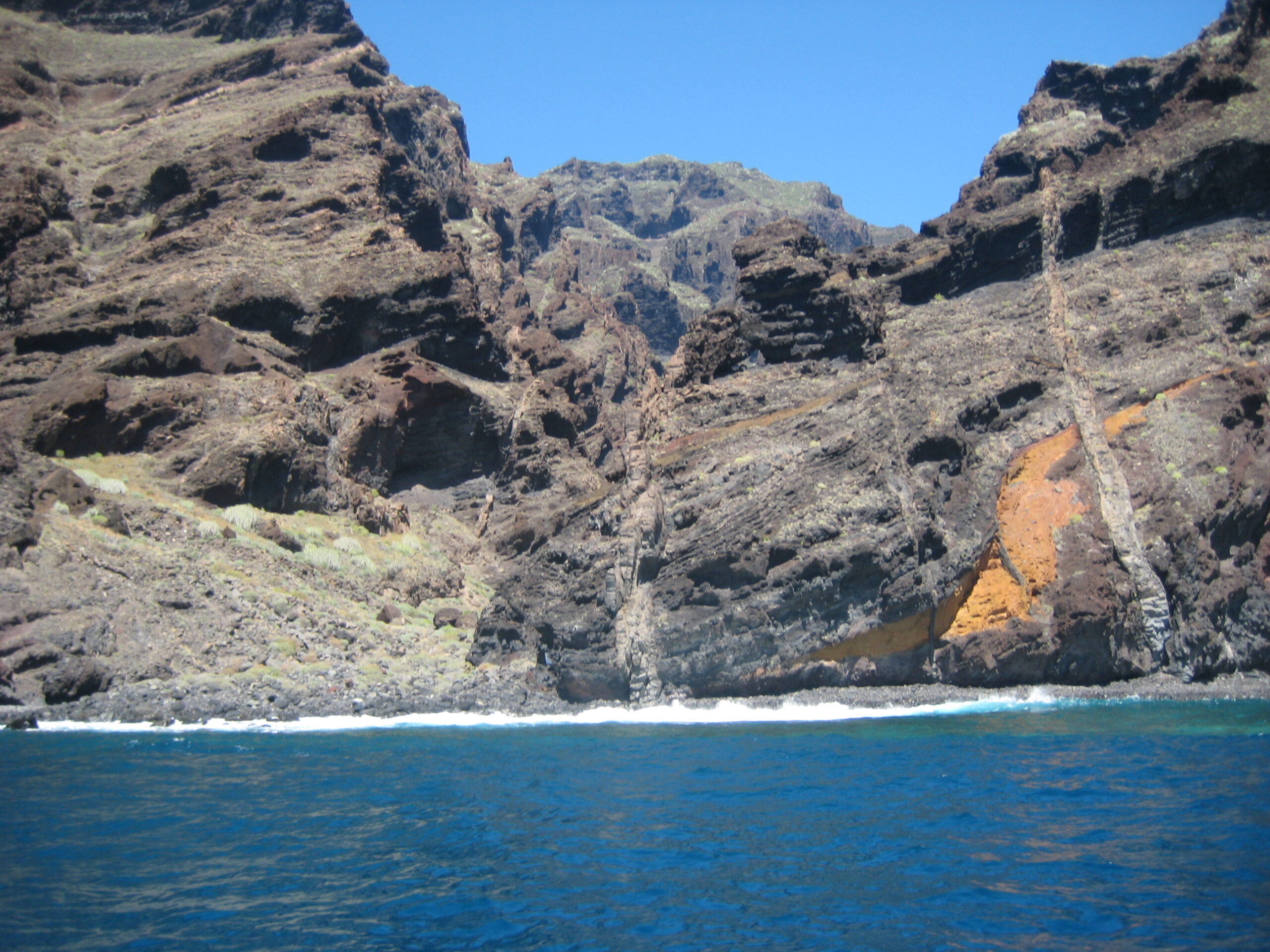 Playa de Masca's striking volcanic cliffs plunge into crystal-clear waters, revealing layers of dark basalt and mineral-rich deposits along Tenerife's rugged coastline.
