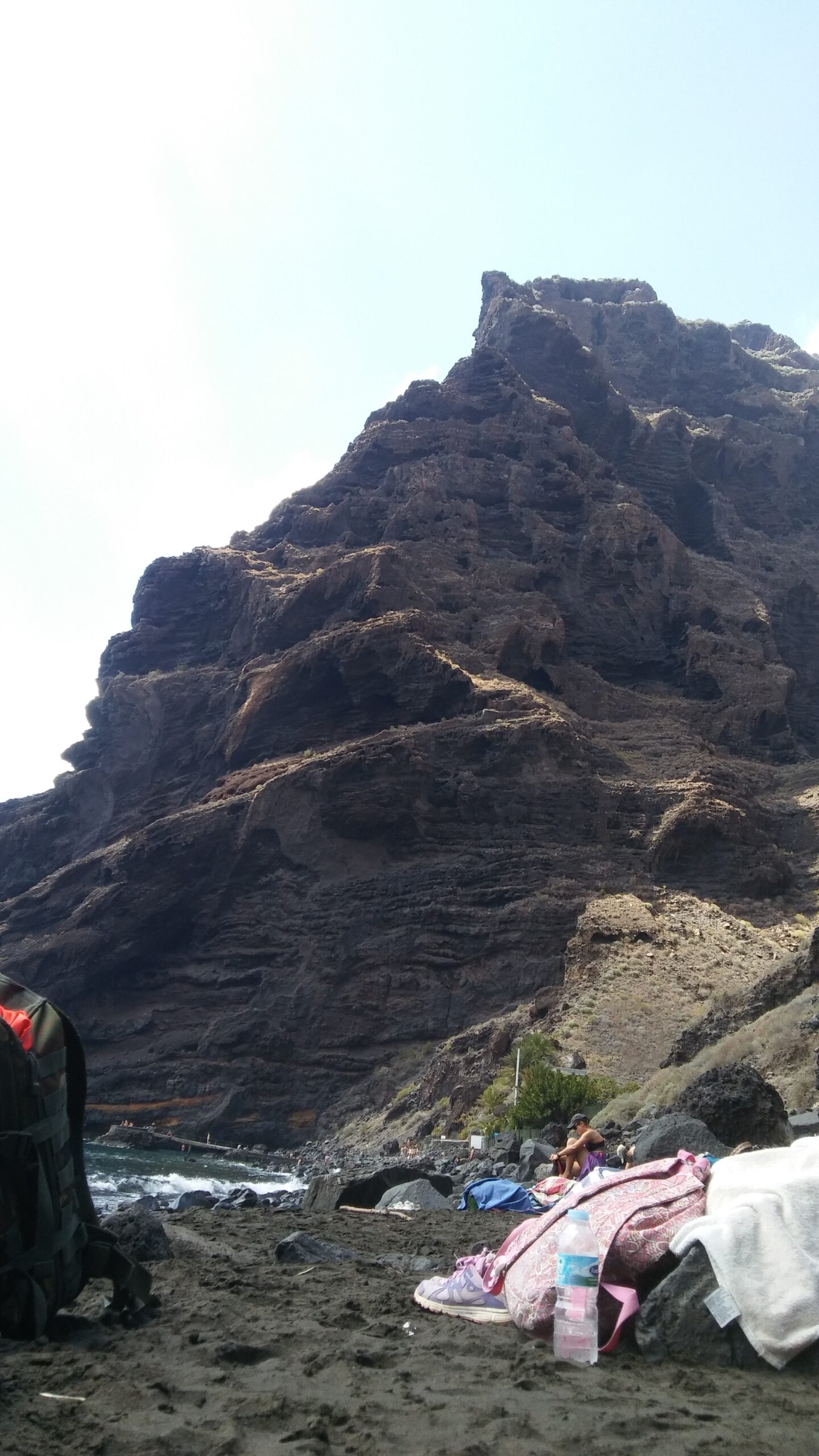 A striking volcanic rock formation towers above Playa de Masca's black sand beach, a popular swimming spot nestled in a coastal valley.