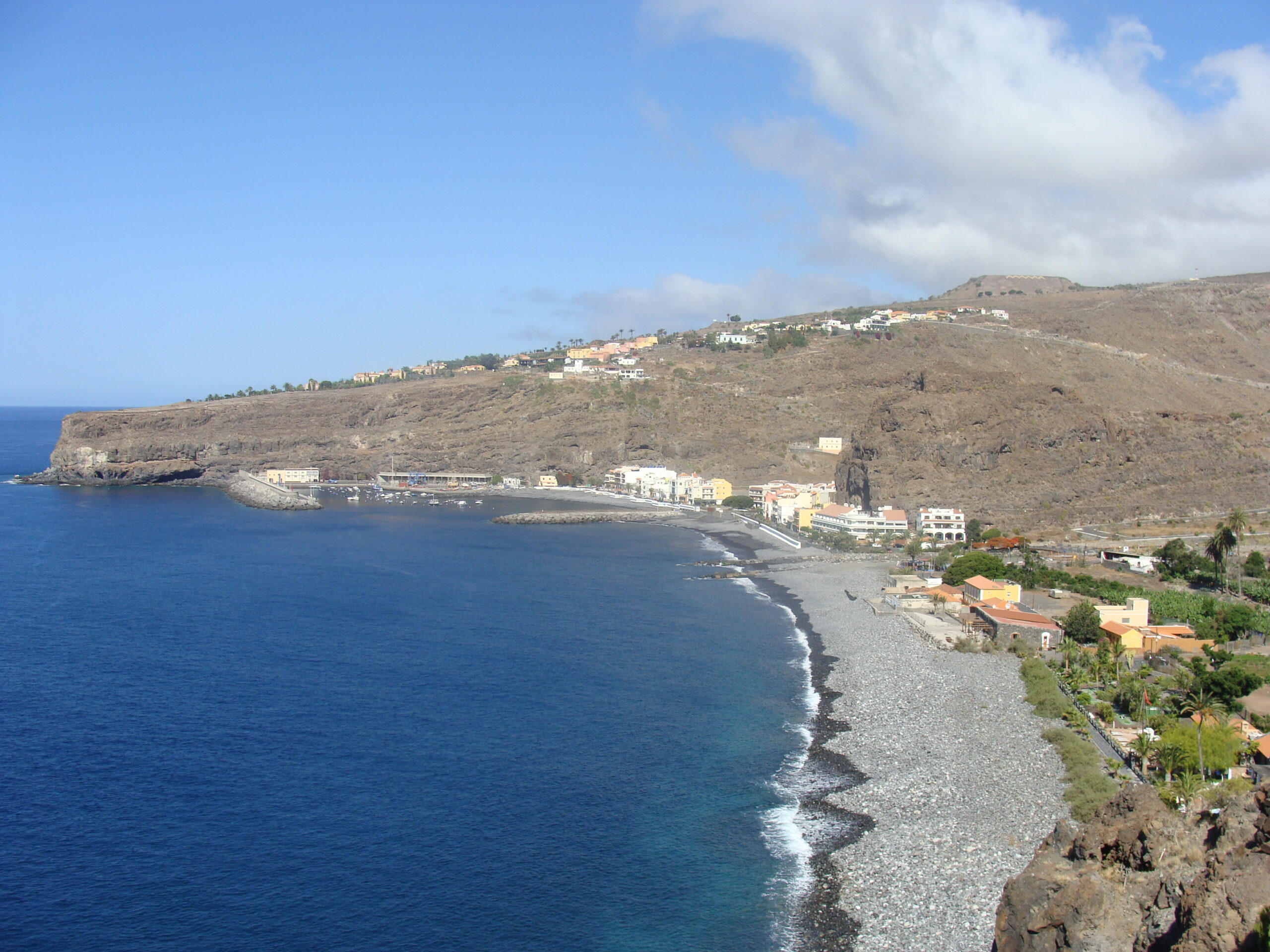 Playa de Santiago curves along a sheltered cove with its characteristic dark volcanic sand beach, backed by terraced buildings and dry hillsides.