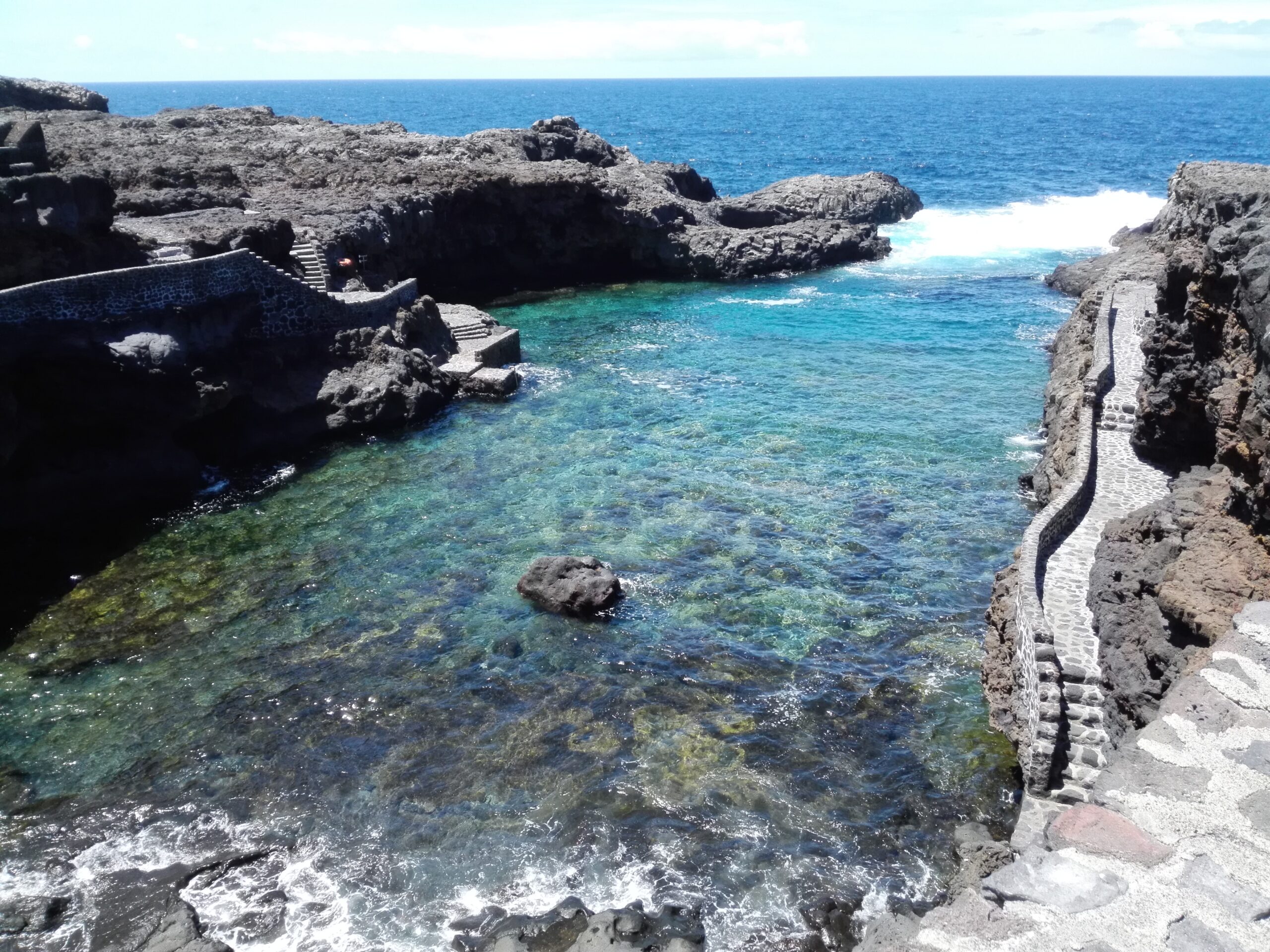 Playa de Tacorón's crystal-clear waters nestle between rugged volcanic cliffs, with carved stone steps providing access to this secluded beach.