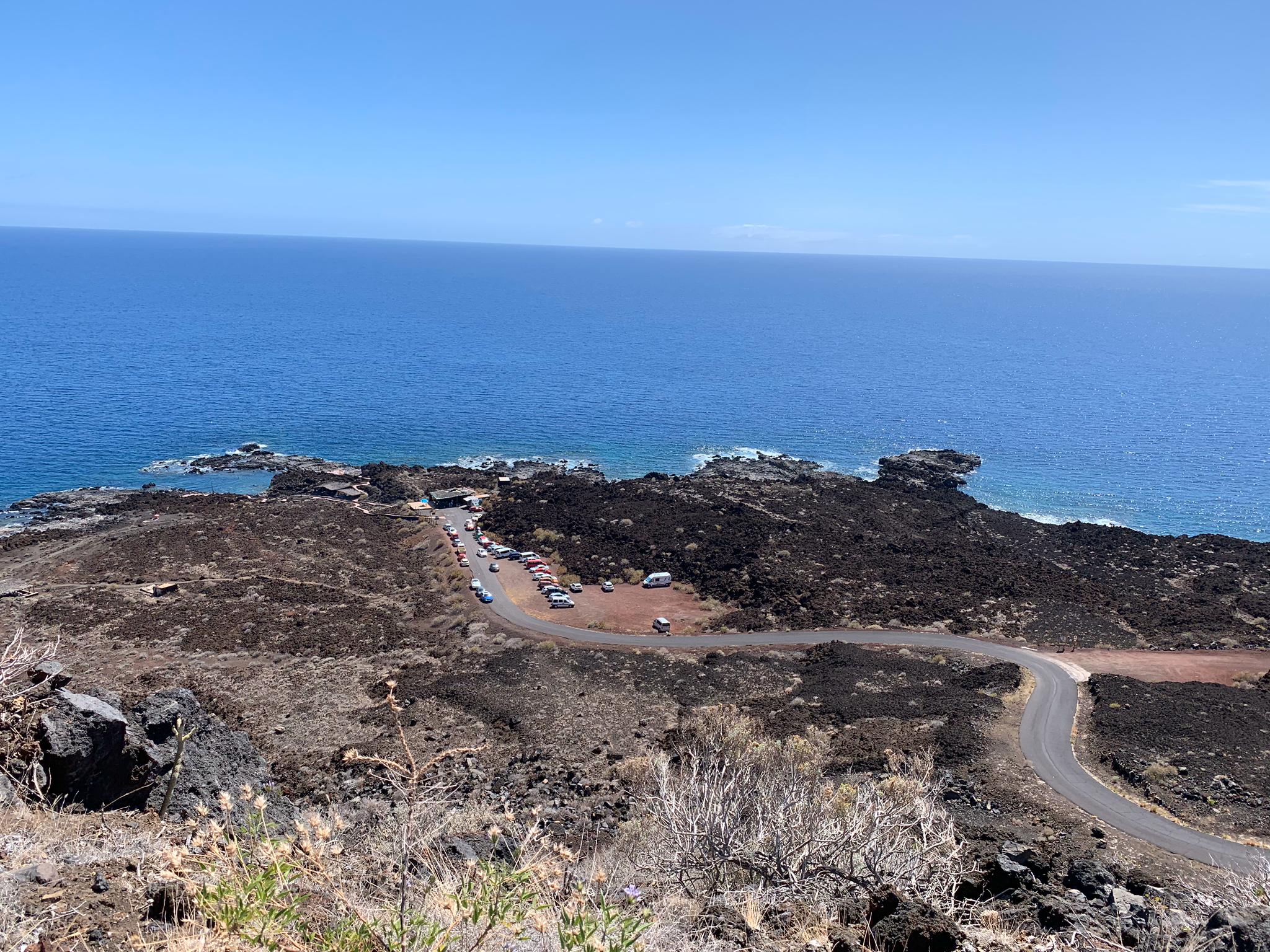 Playa de Tacorón features a dramatic volcanic landscape with dark basalt rock formations framing the turquoise waters below.