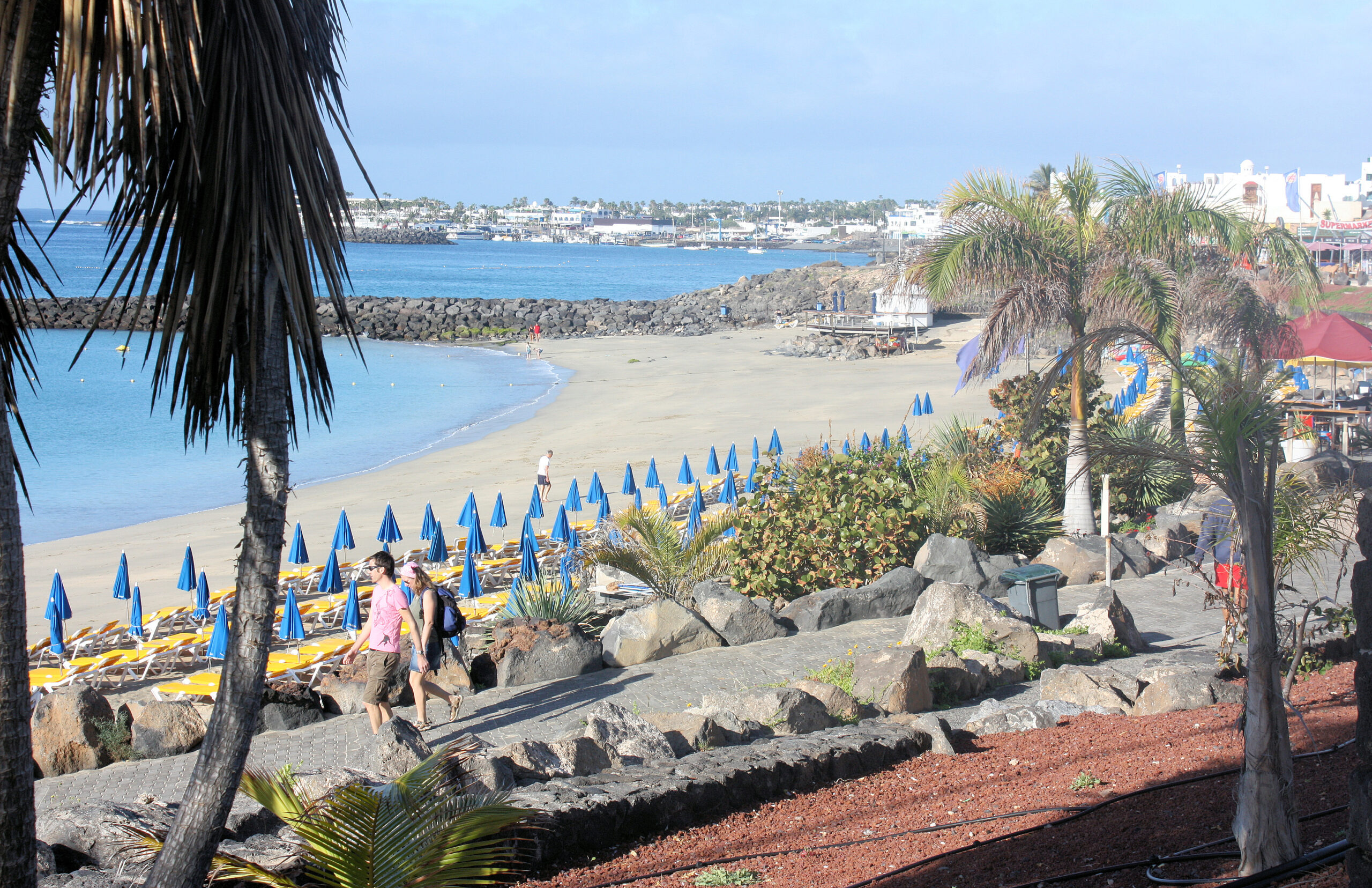 Playa Dorada in Playa Blanca offers a sheltered sandy beach lined with blue umbrellas and loungers, backed by palm-fringed promenades and views of the town's whitewashed architecture.