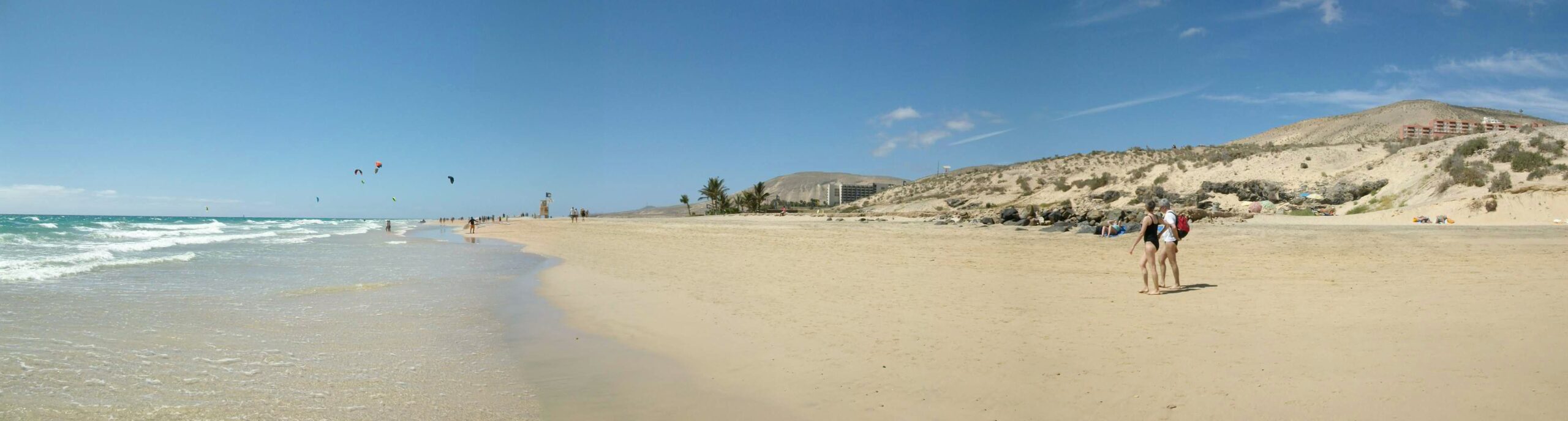 Playa Esmeralda stretches along Fuerteventura's southern coast with soft sand, gentle waves, and dramatic dune formations rising behind the shoreline.