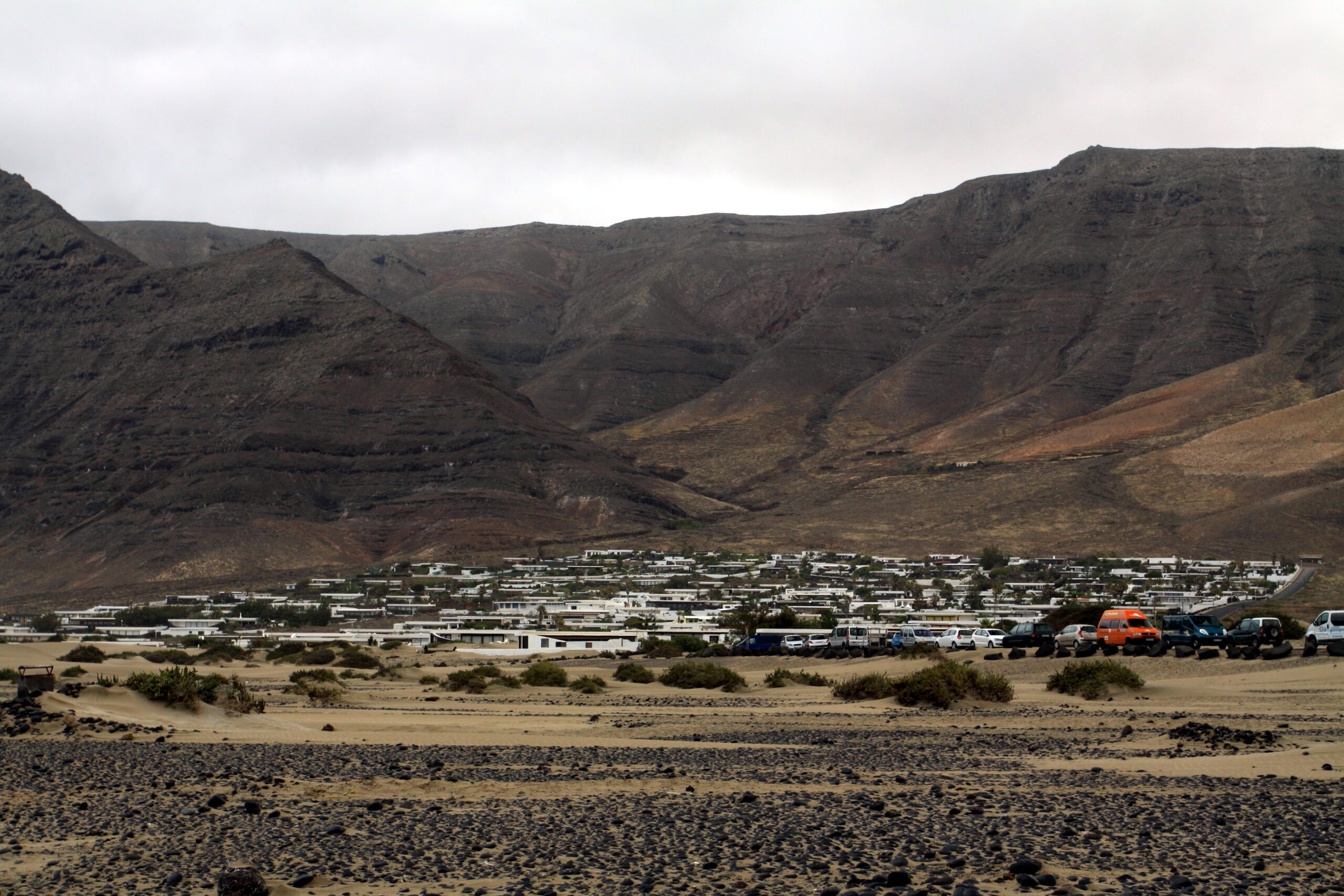 The beach settlement of Famara spreads across the sandy valley floor, backed by dramatic volcanic ridges and mountains characteristic of Lanzarote's stark landscape.