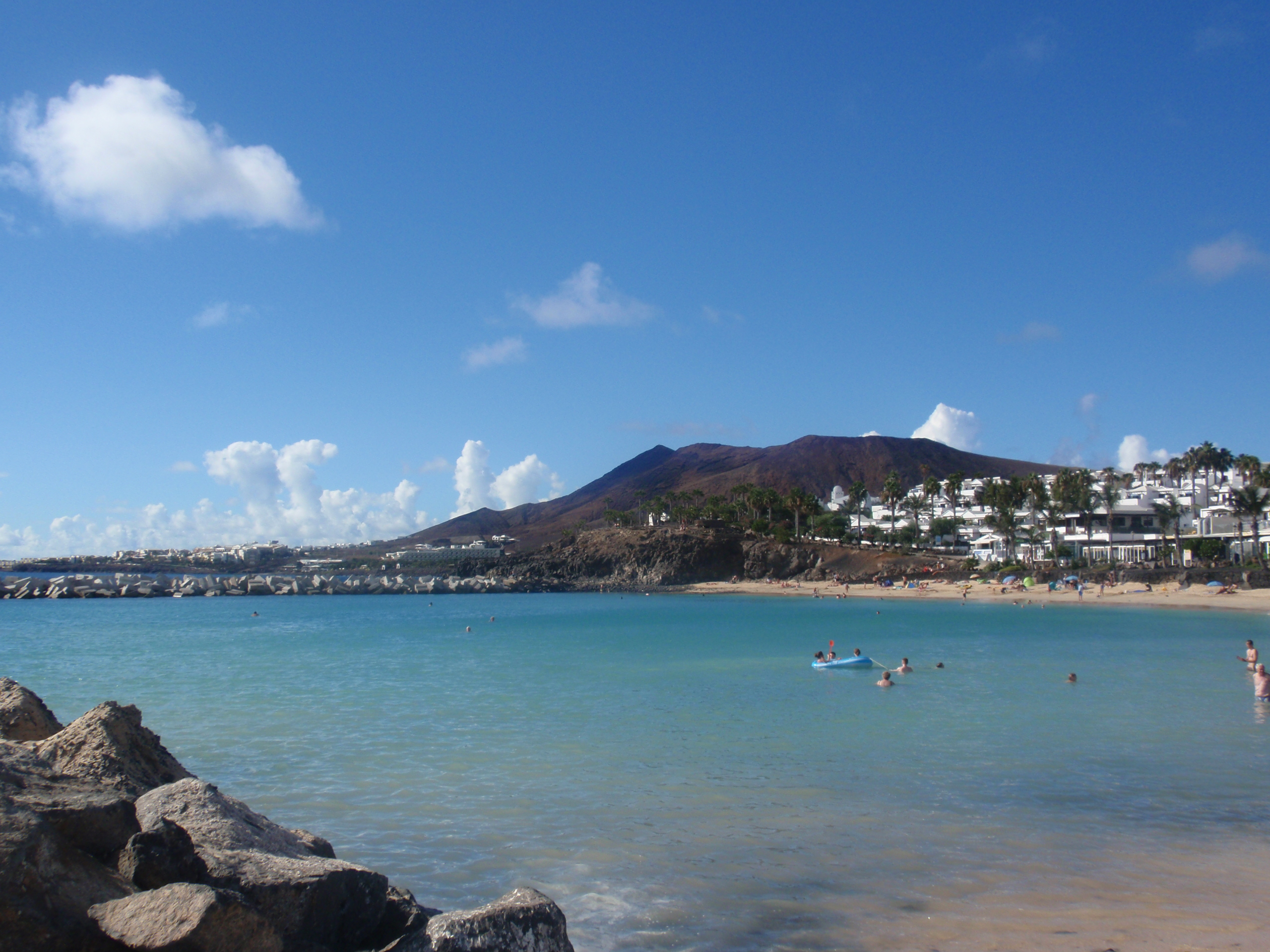 Playa Flamingo's sheltered cove features calm turquoise waters, a sandy beach backed by whitewashed development, and the distinctive volcanic cone of Montaña Roja rising beyond.