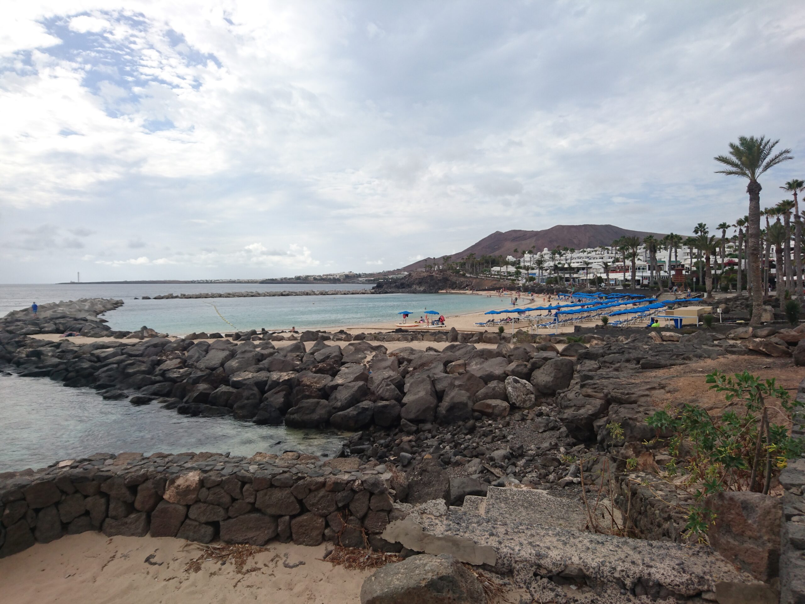 Playa Flamingo curves along the coast with natural rock formations and palm-lined promenade, overlooking the calm turquoise waters and volcanic landscape beyond.