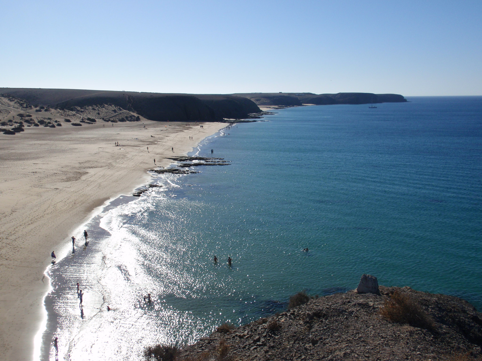 Playa Mujeres features pristine golden sand, crystalline turquoise waters, and dramatic volcanic cliffs rising above the shoreline.