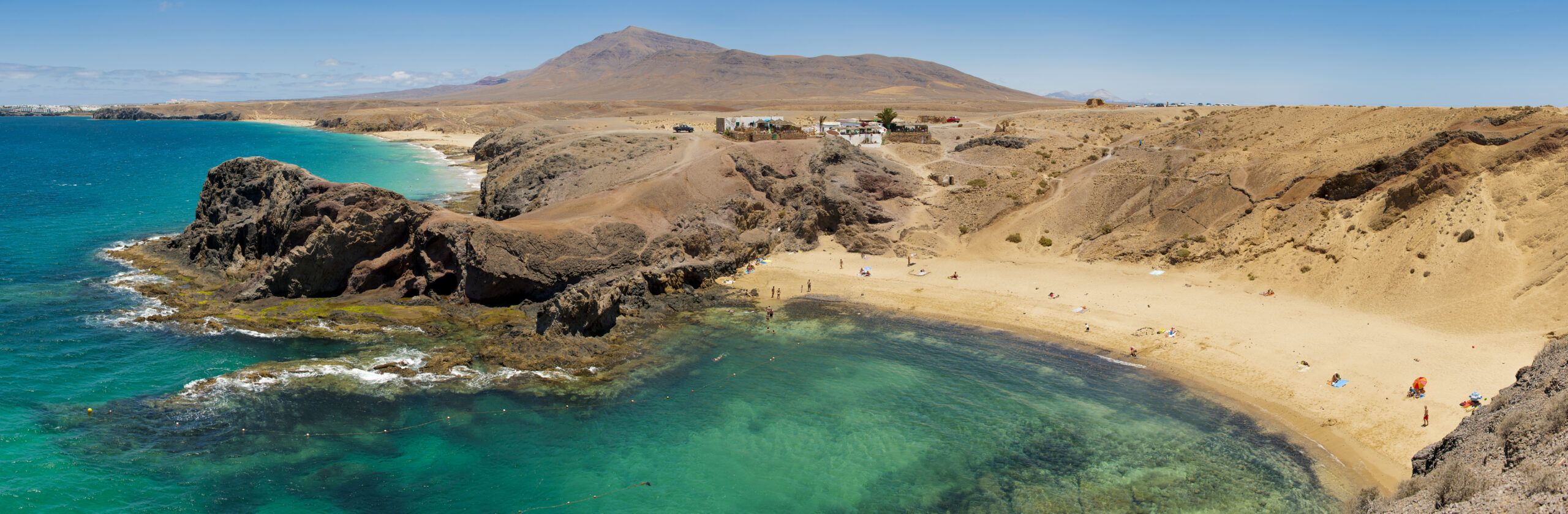 Playa Papagayo's crystalline turquoise waters and sheltered sandy cove are framed by dramatic volcanic terrain and views toward Fuerteventura's peaks.