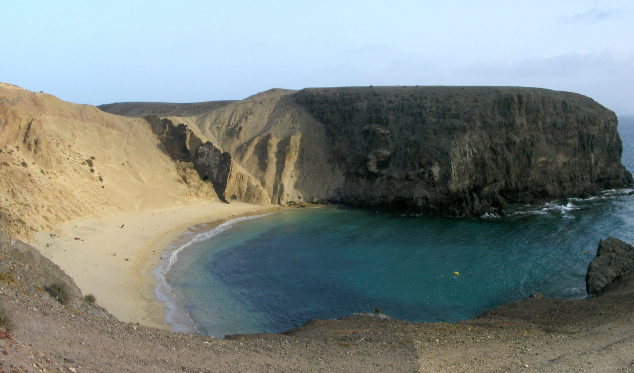 Playa Papagayo's sheltered cove features golden sand, clear turquoise waters, and dramatic volcanic cliffs rising steeply on three sides.