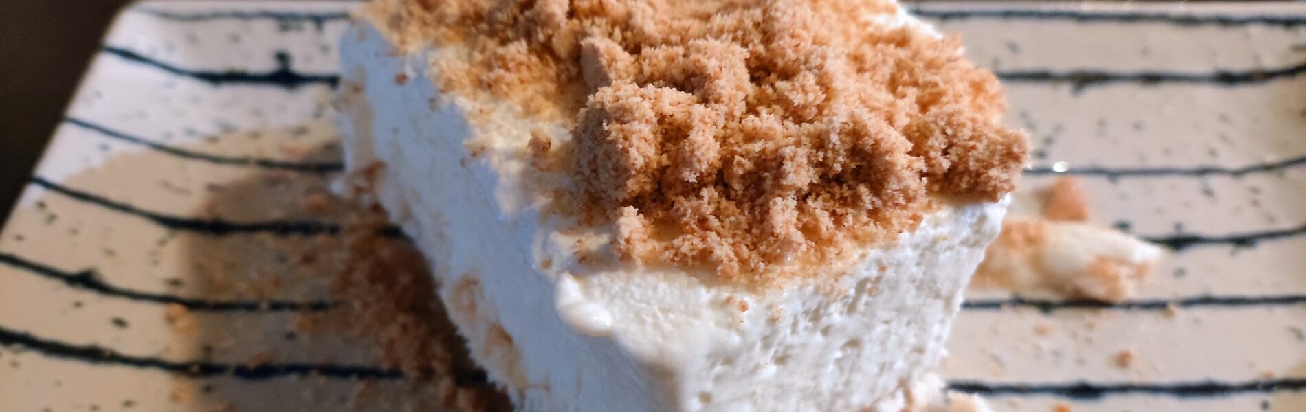 Slice of creamy white cake topped with cinnamon powder on a striped plate