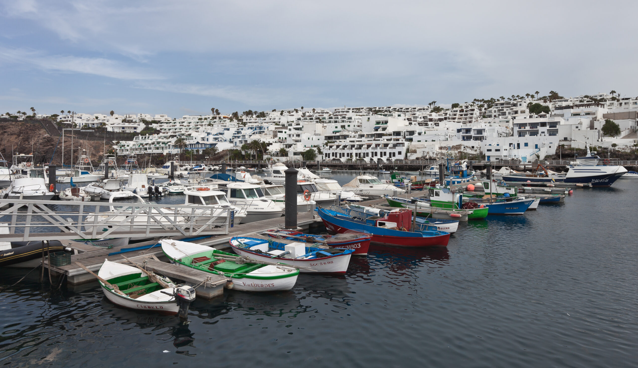 The picturesque harbor of Puerto del Carmen features traditional fishing boats in bright blues, greens, and reds against a backdrop of whitewashed architecture.