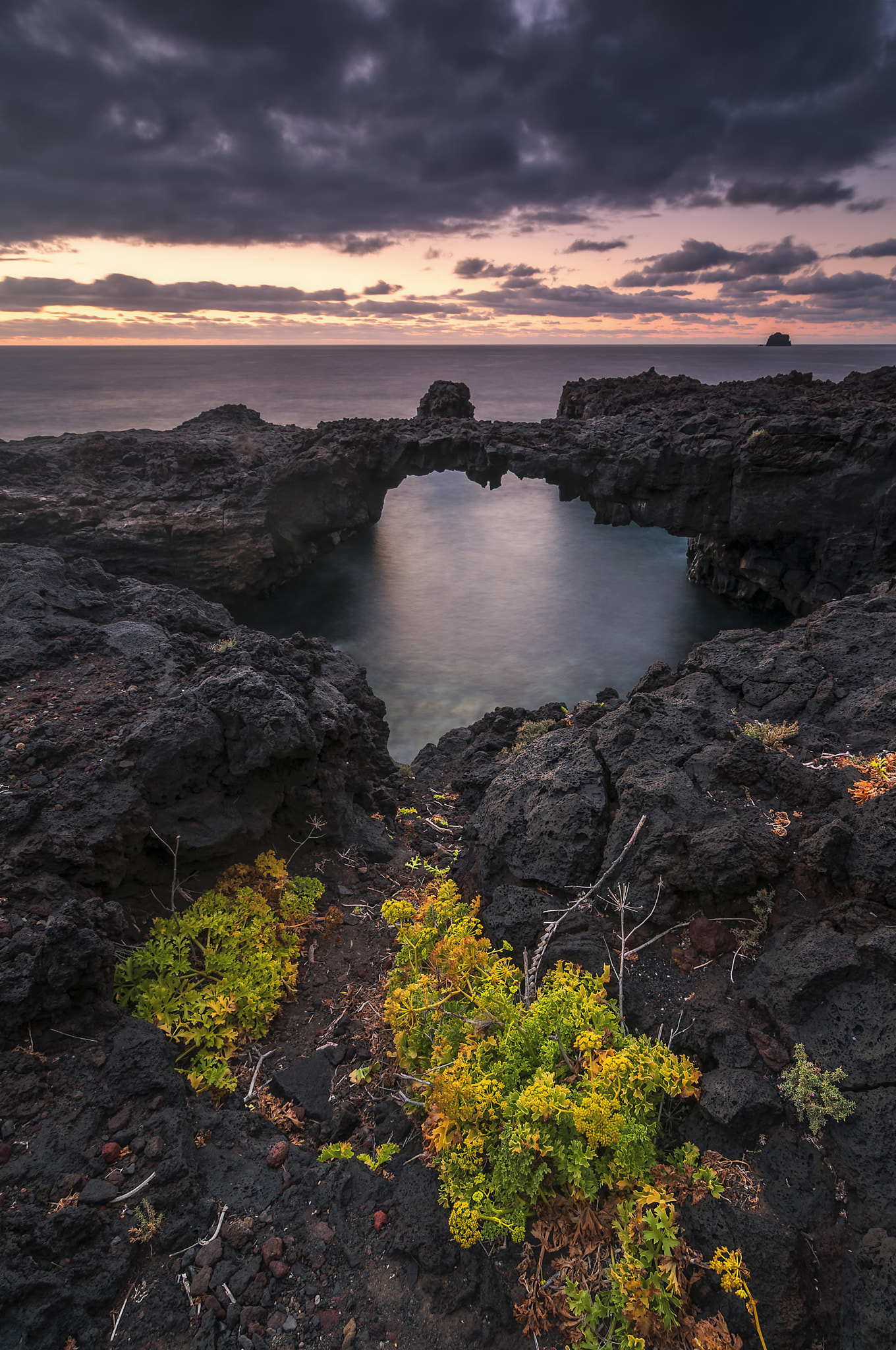 A sheltered natural pool nestled among El Hierro's rugged volcanic rocks offers a serene view toward the horizon as evening clouds gather.