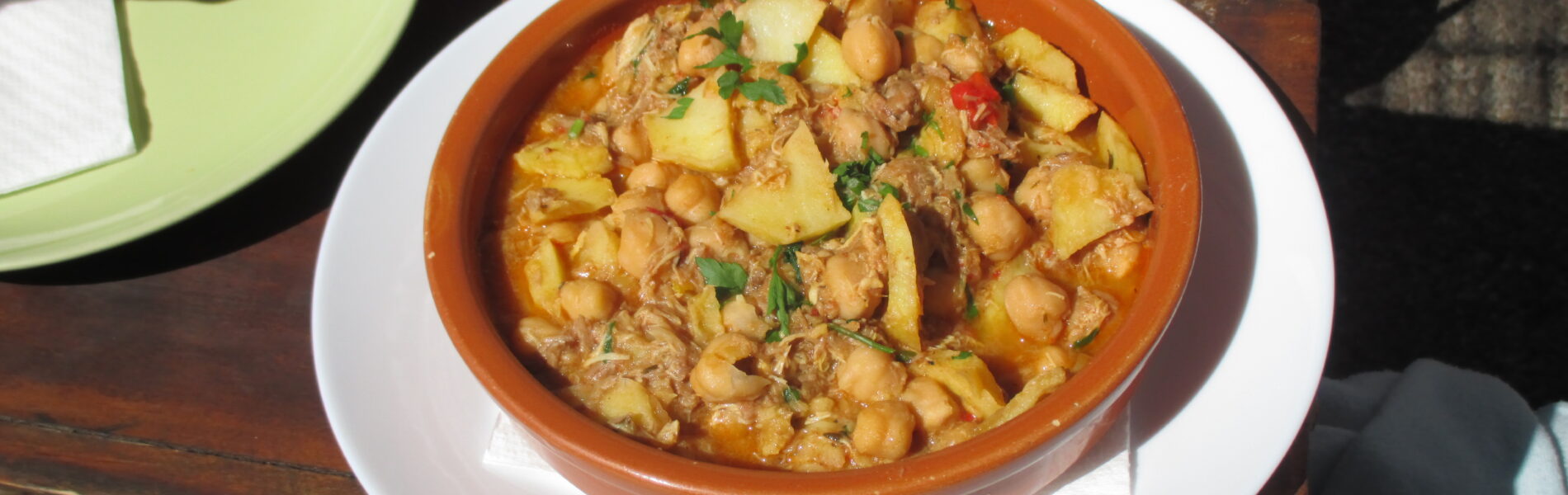 Ropa vieja canaria in a terracotta bowl on a white plate, topped with fresh parsley, served outdoors on a wooden table