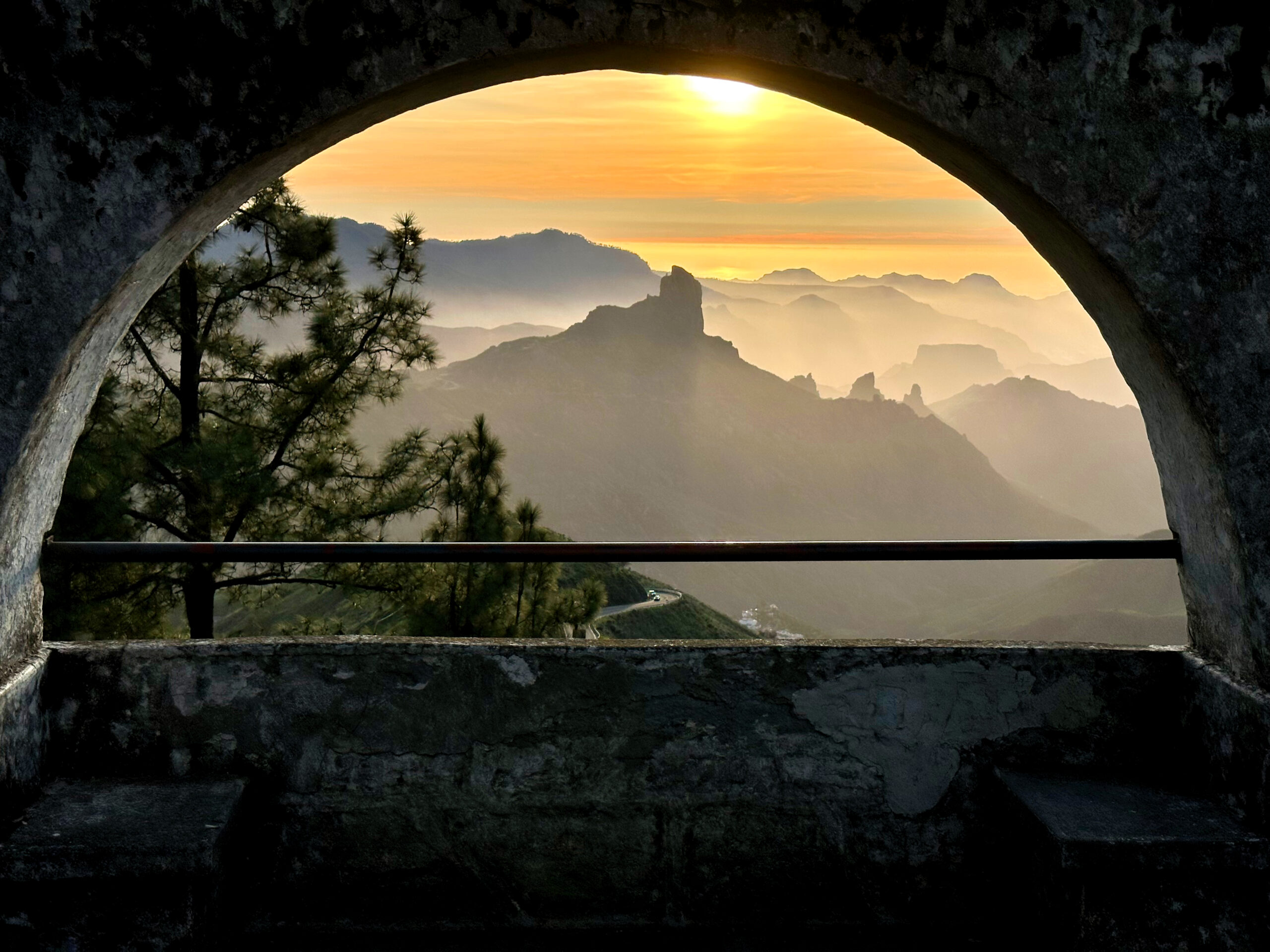 The dramatic volcanic peaks of Gran Canaria's interior framed through a stone viewpoint arch at Roque Bentayga, with morning mist settling in the valleys below.