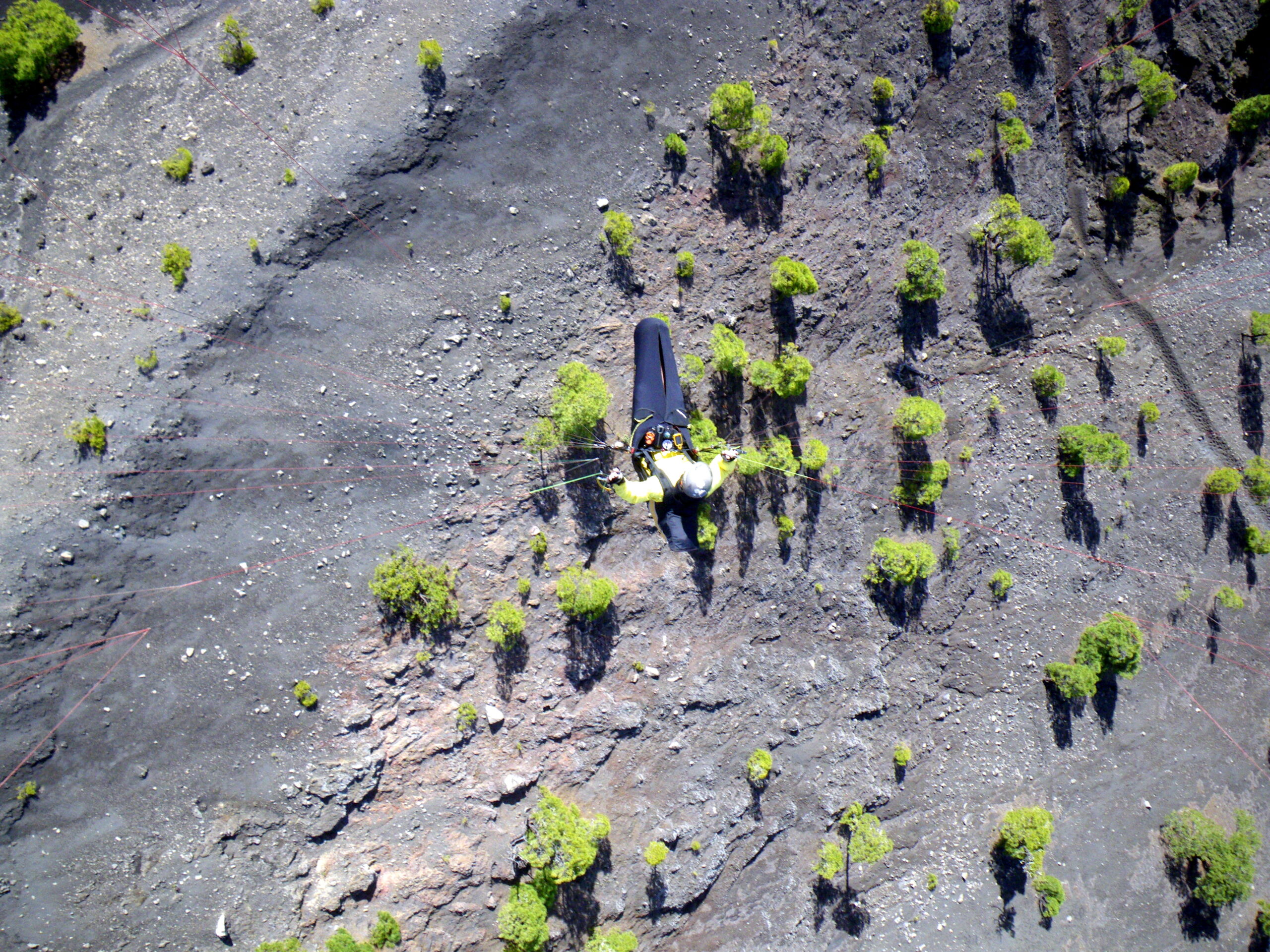 A solitary hiker traverses the stark volcanic landscape of Cumbre Vieja, where sparse vegetation clings to the dark lava fields.