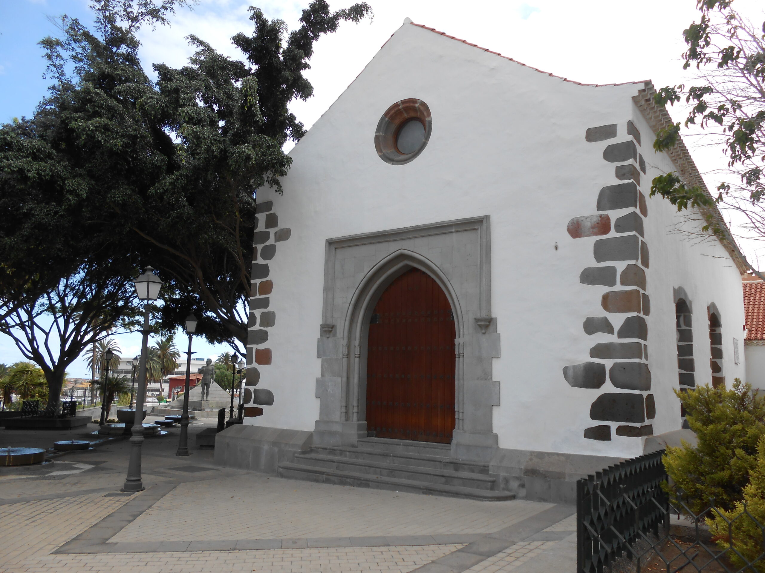 San Juan Church in Telde features distinctive whitewashed walls trimmed with dark basalt stone and a prominent red wooden entrance door.
