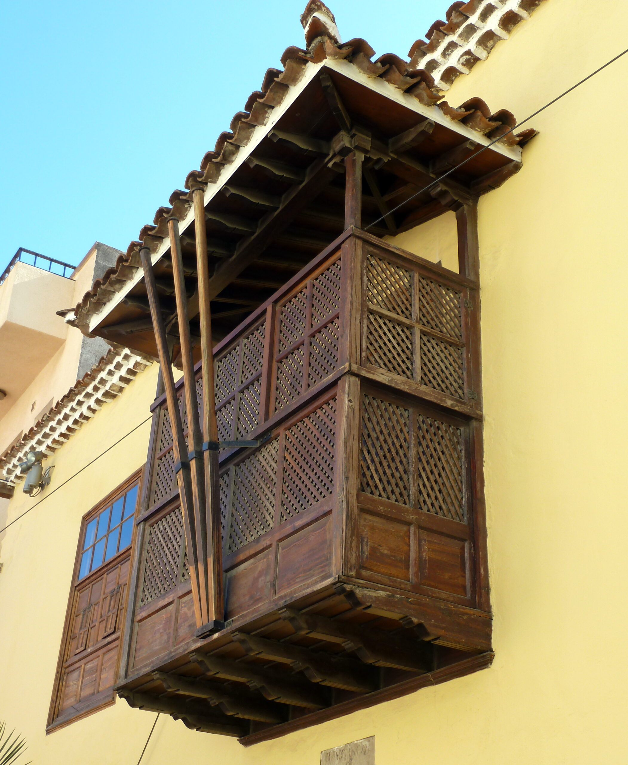 A traditional wooden balcony with intricate latticed screens and decorative carved eaves exemplifies the colonial architecture found in San Sebastián’s historic old town.