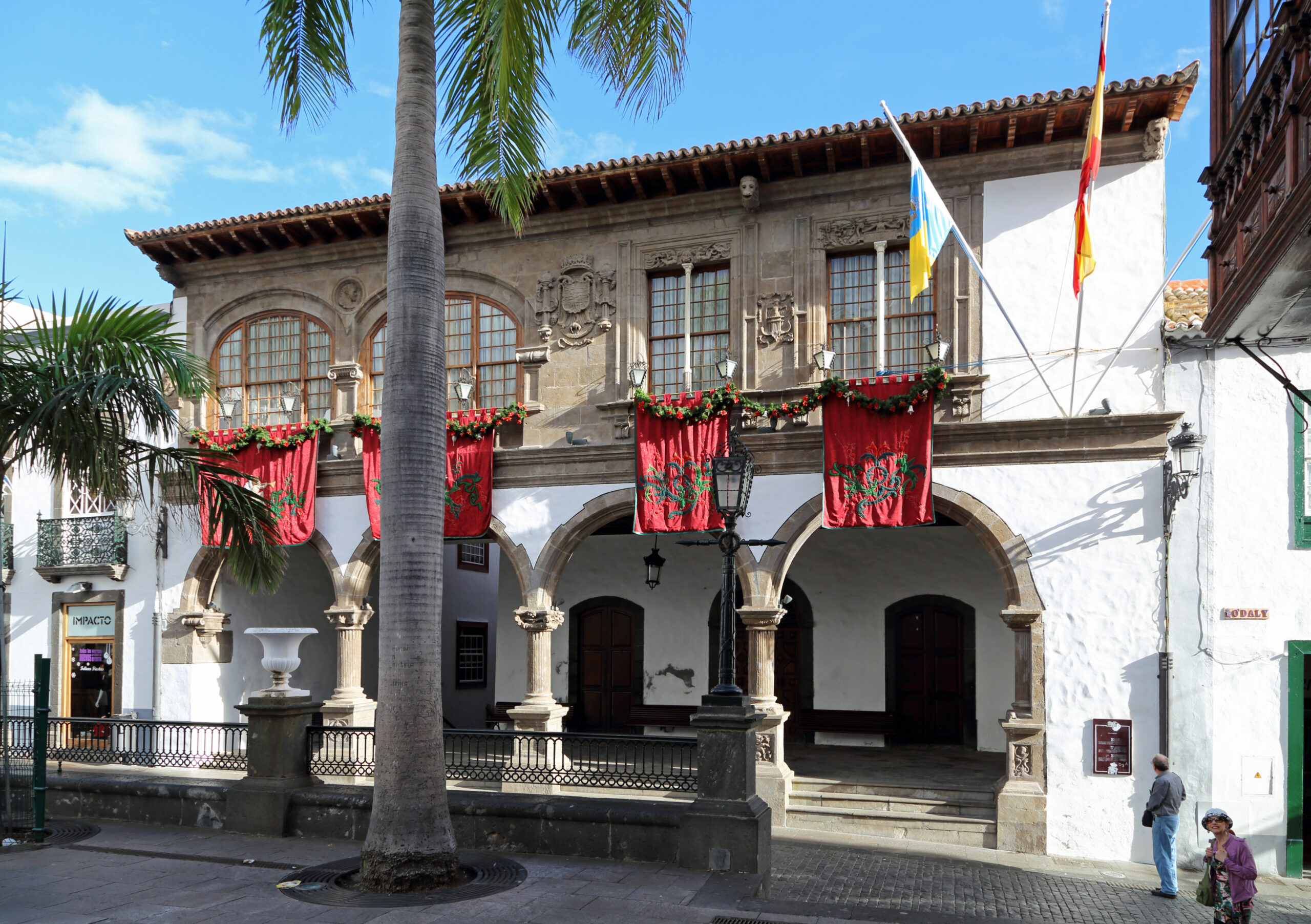 The historic Casa de los Salazar in Santa Cruz de La Palma's Old Town, featuring characteristic colonial architecture with stone arcades and festive red floral decorations.