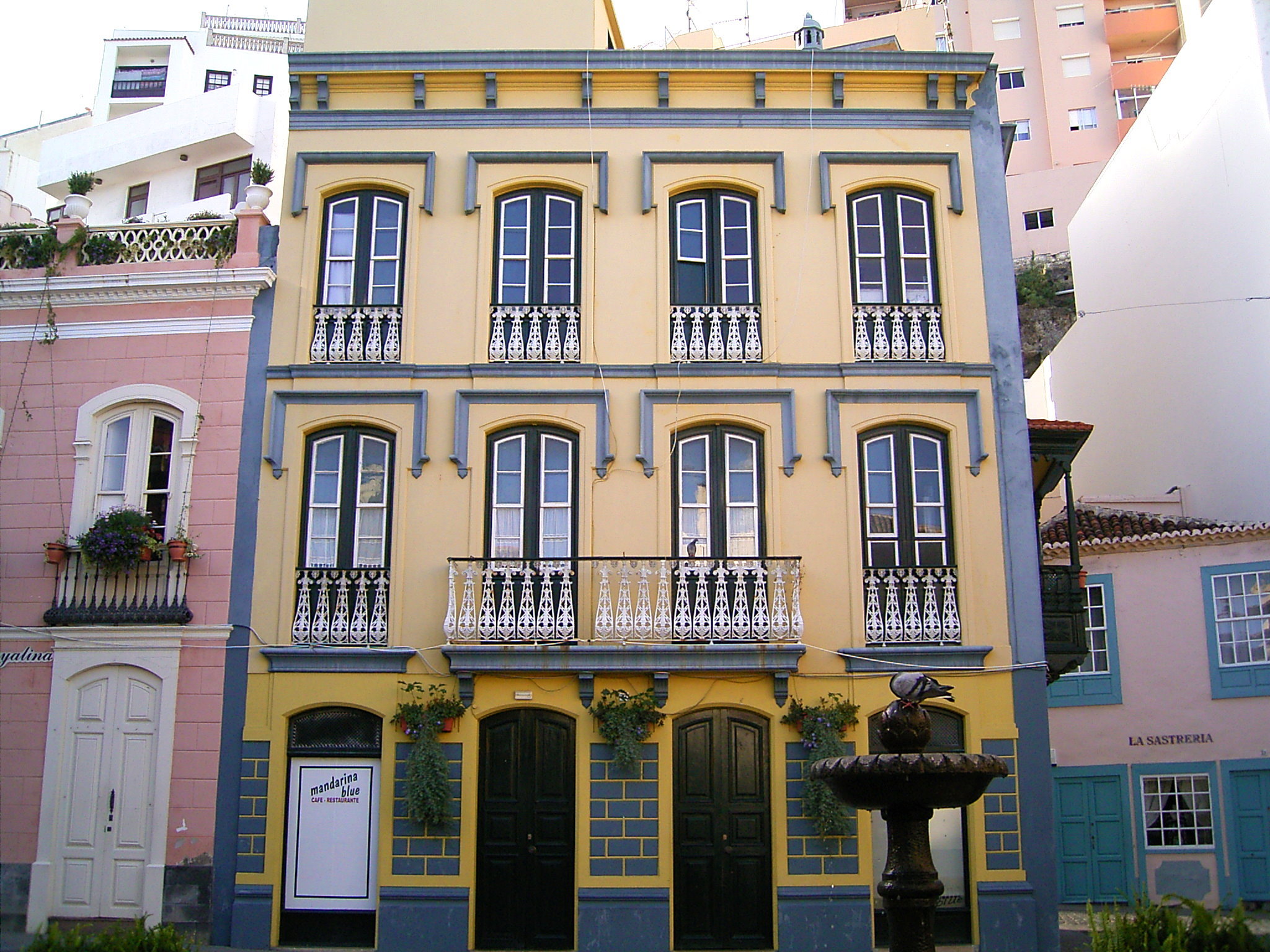 A striking colonial-era mansion in Santa Cruz de La Palma's Old Town, painted in bright yellow and blue with ornate iron railings on its upper-floor balconies.