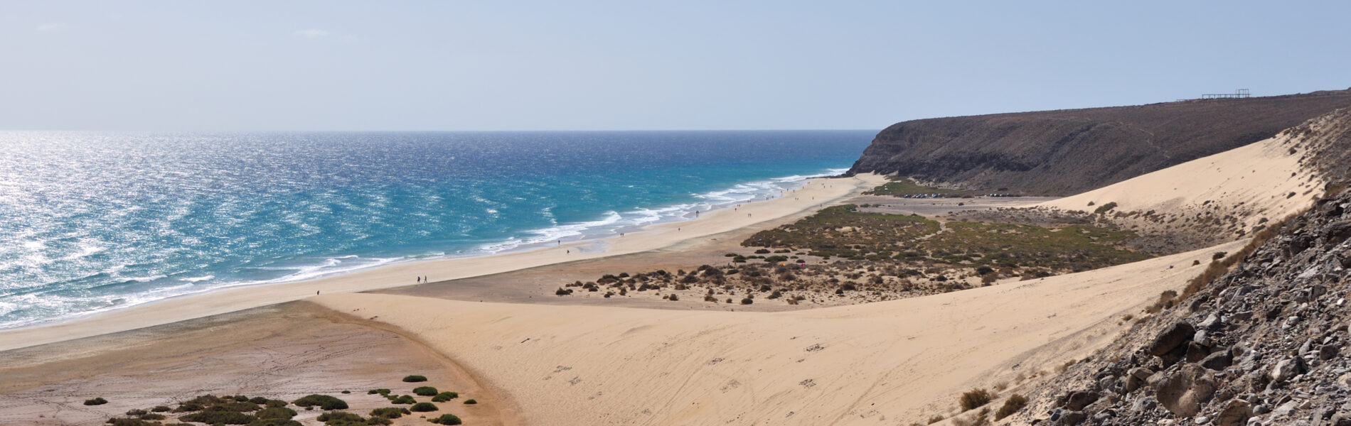 Sotavento Beach with golden sand, turquoise waters, and dark volcanic cliffs under clear blue sky