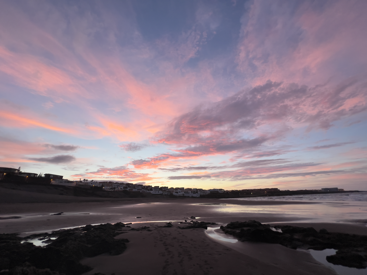 Warm sunset colours illuminate the Telde coastline, with volcanic rock formations and whitewashed waterfront buildings.