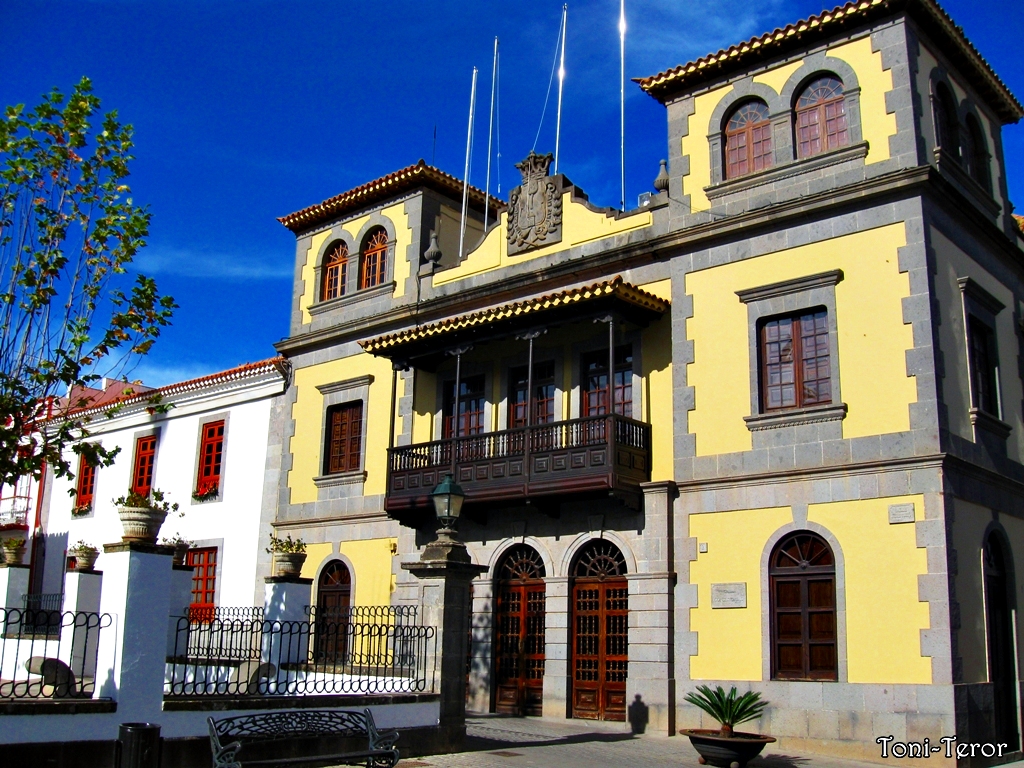 A striking yellow colonial mansion in Teror features traditional Canarian architecture with wooden balconies and decorative stonework.