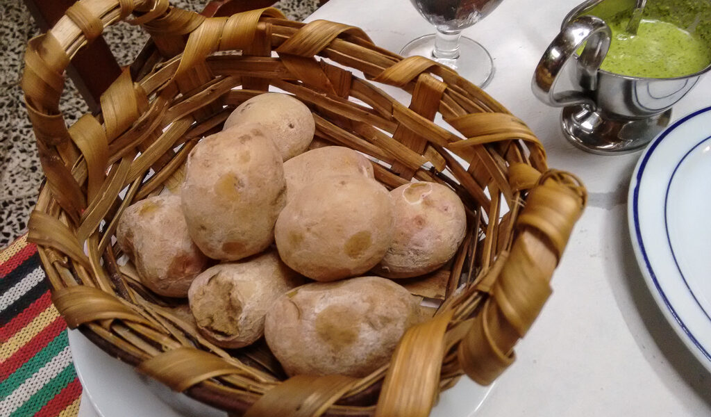 Woven wooden basket holding several unpeeled potatoes on a white plate at a dining table