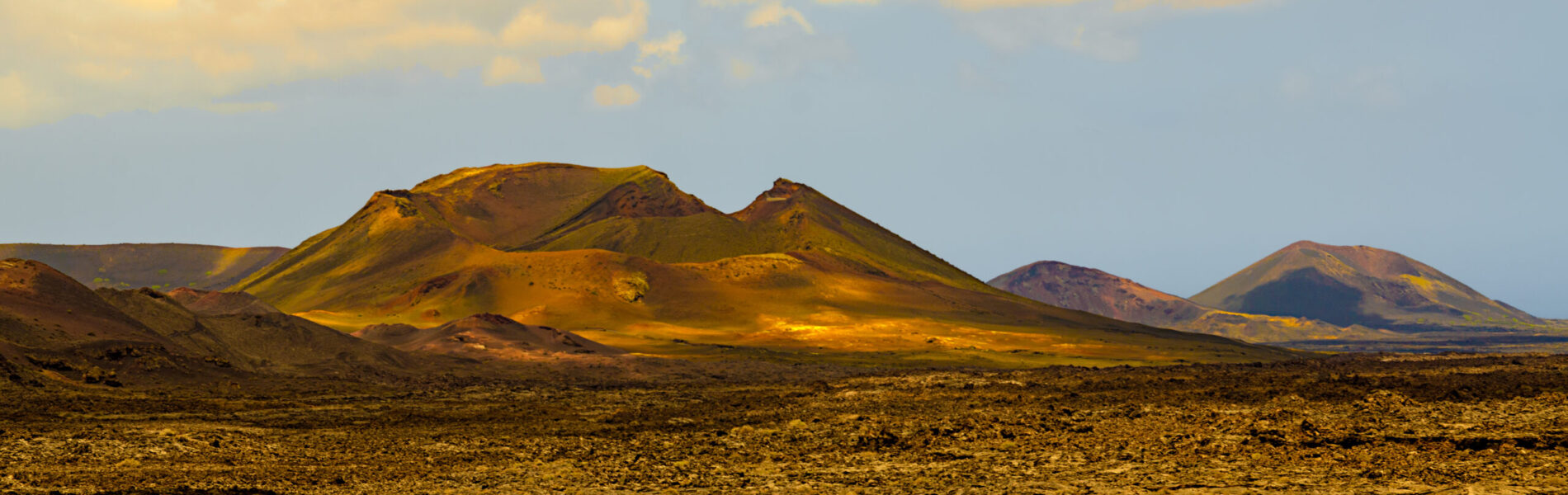 Golden-hued volcanic cones rising from dark lava plains under partly cloudy sky