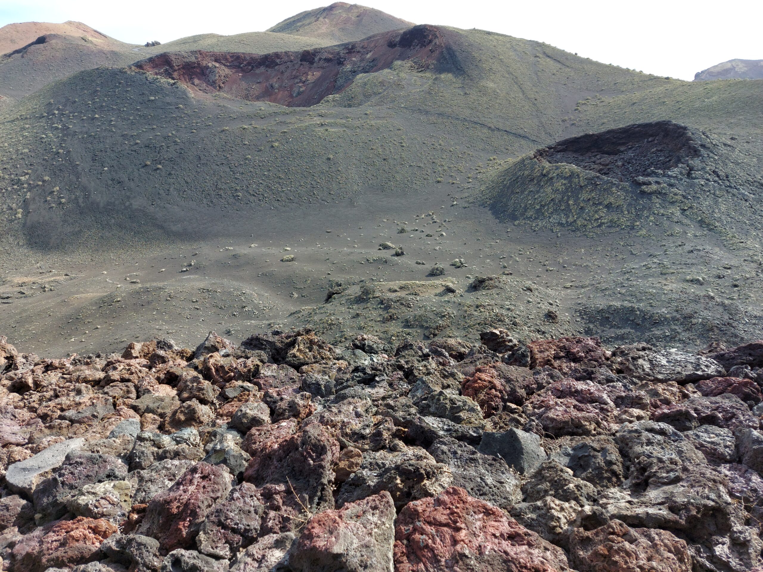 The stark volcanic terrain of Timanfaya National Park displays dormant cinder cones and scattered lava fields characteristic of Lanzarote's geothermal landscape.