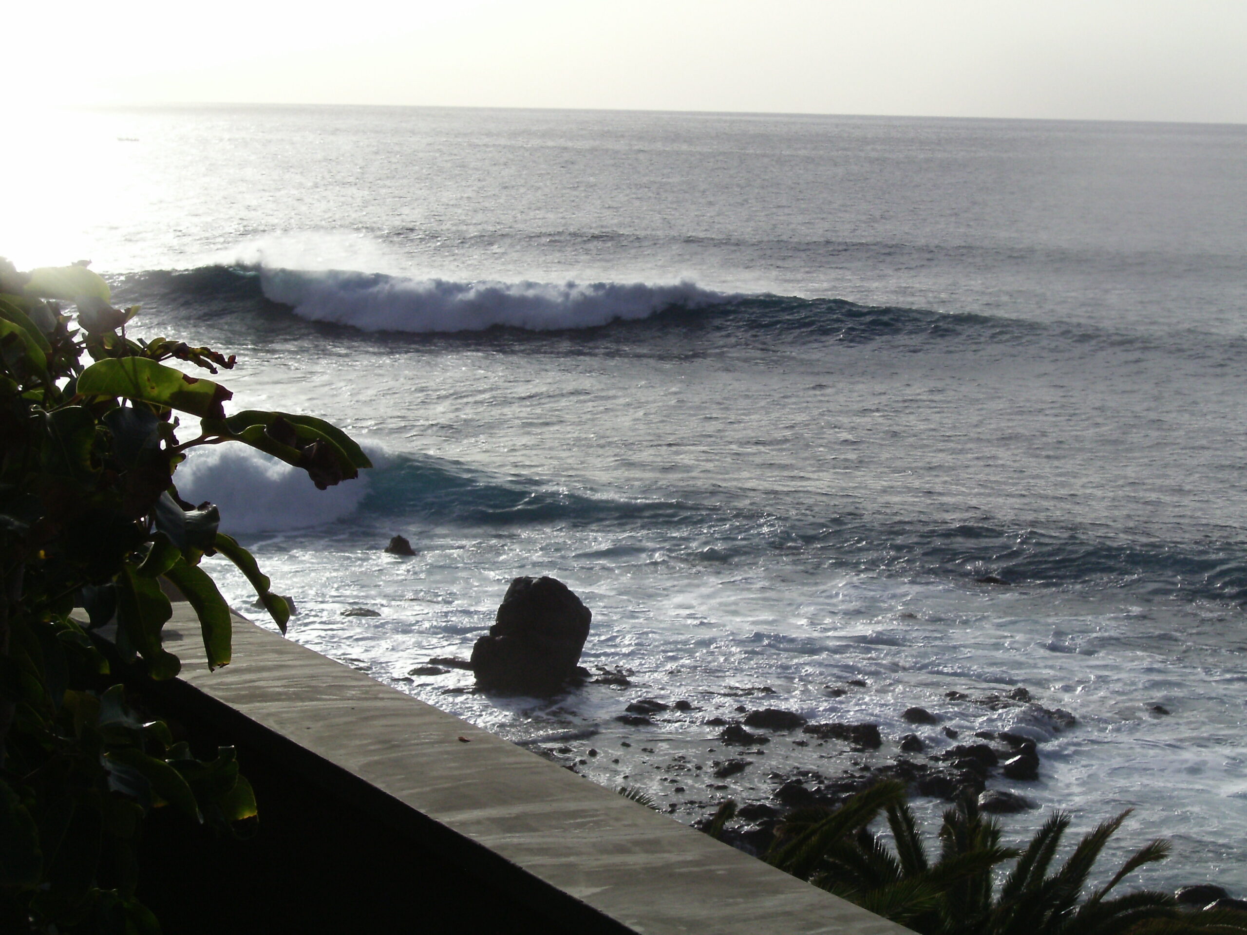 Valle Gran Rey Beach features dramatic Atlantic waves rolling onto a rocky shoreline framed by lush coastal vegetation.