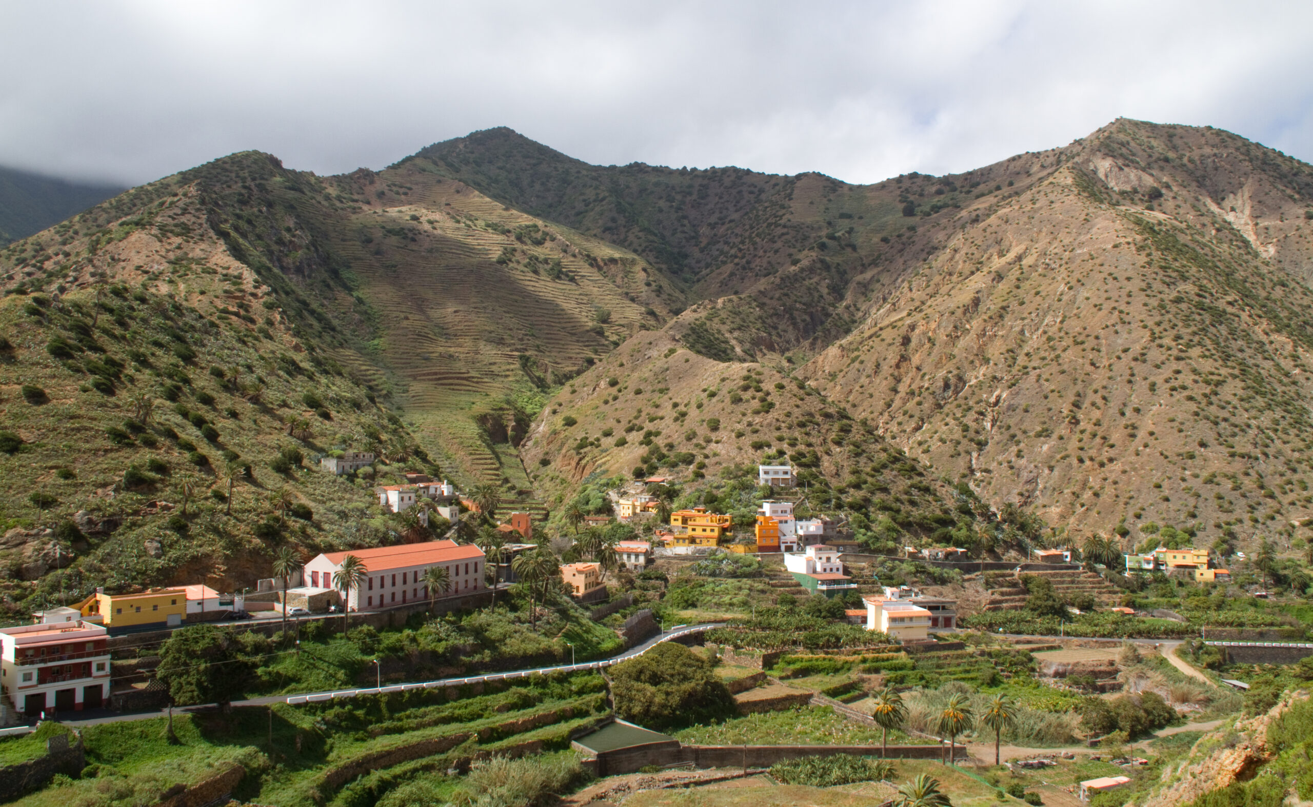 Vallehermoso spreads across a lush valley floor on La Gomera, with colorful buildings and palm groves backed by dramatic volcanic peaks.