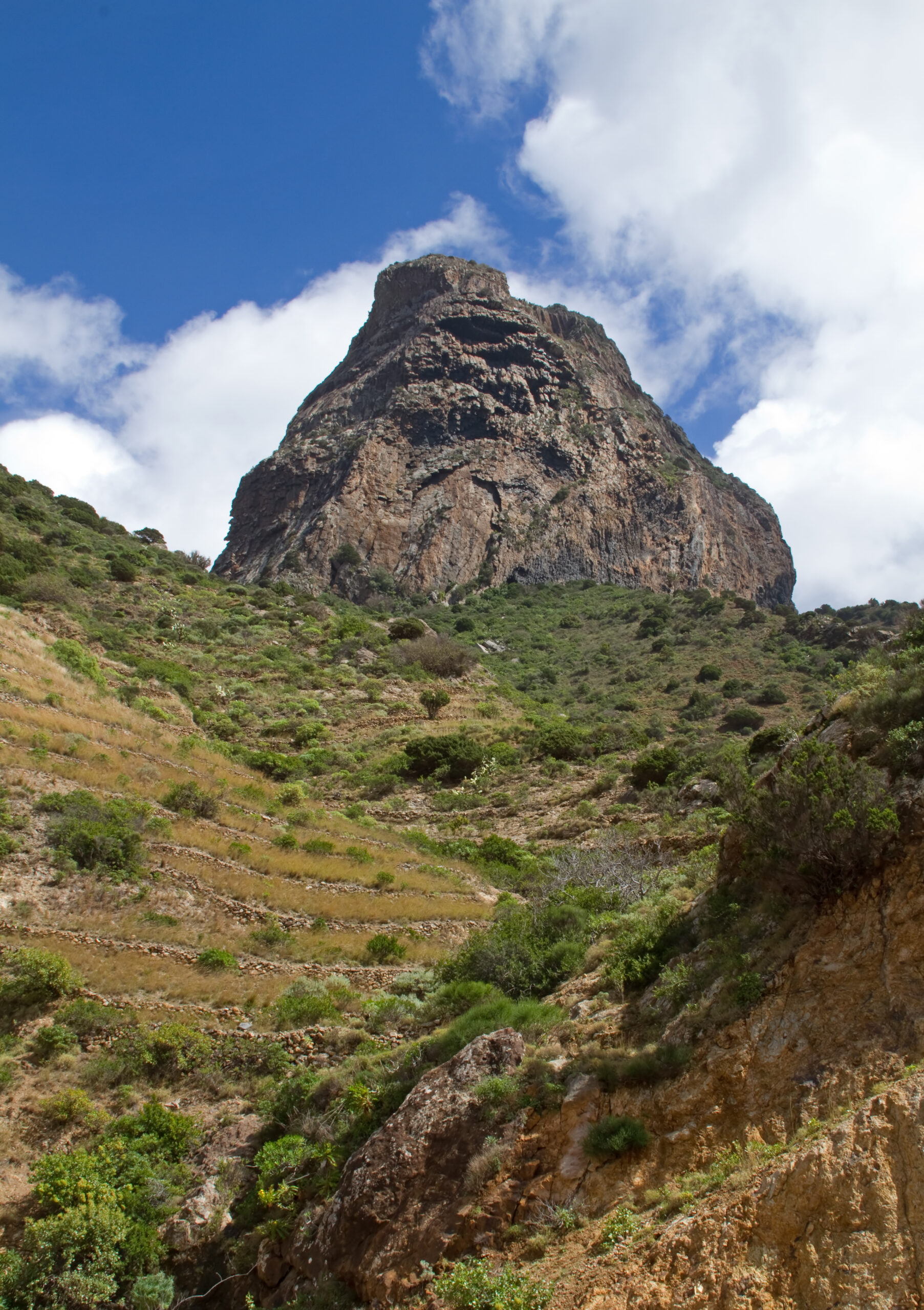 A dramatic volcanic rock formation dominates the landscape above Vallehermoso, surrounded by green hillside vegetation.