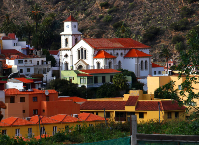 The parish church of Vallehermoso dominates the town center, its distinctive white walls and red roof contrasting with the surrounding residential architecture and the arid hillside backdrop.