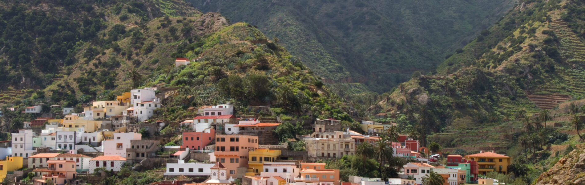 Colorful village houses nestled in a steep mountain valley with green hillsides and misty peaks above.