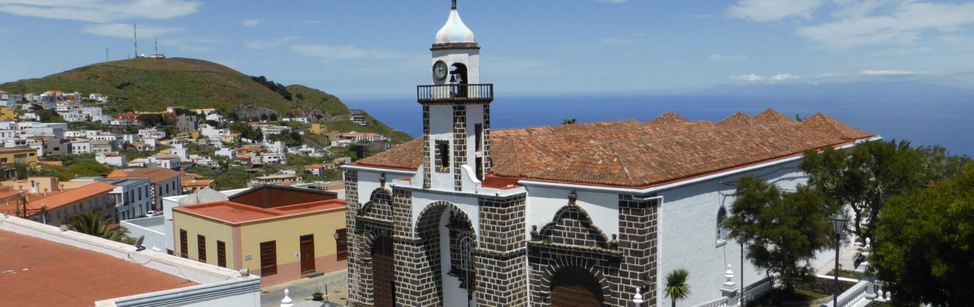 White church with dark stone tower overlooking hillside town and ocean