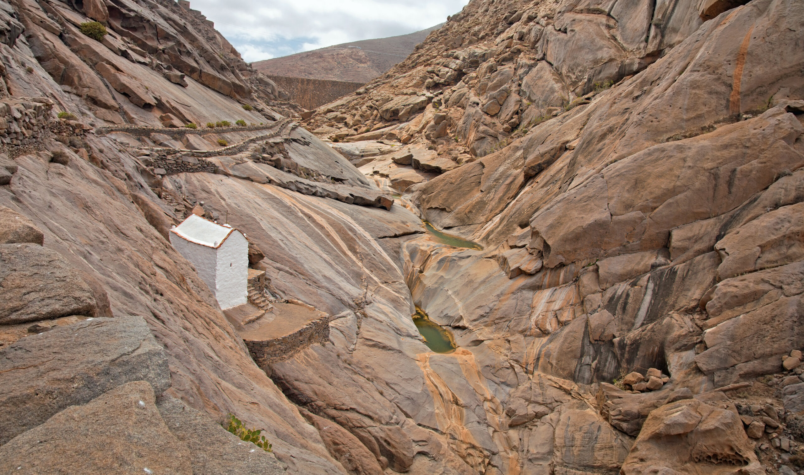 The Vega de Río Palmas gorge features dramatic stratified rock walls and a small white chapel built into the canyon.