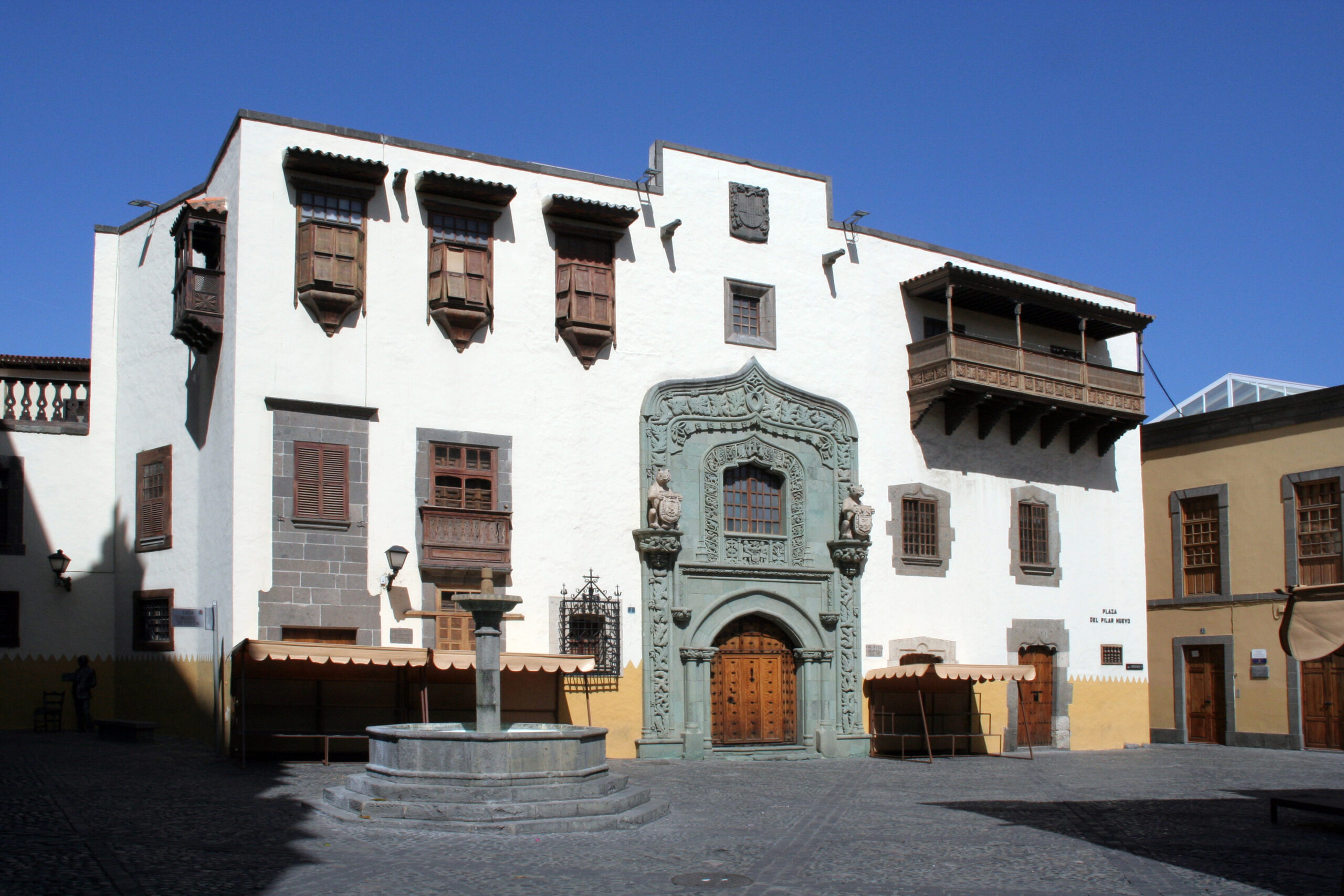 A restored colonial palace in Vegueta, with a carved stone entrance and traditional wooden balconies overlooking a cobbled plaza.
